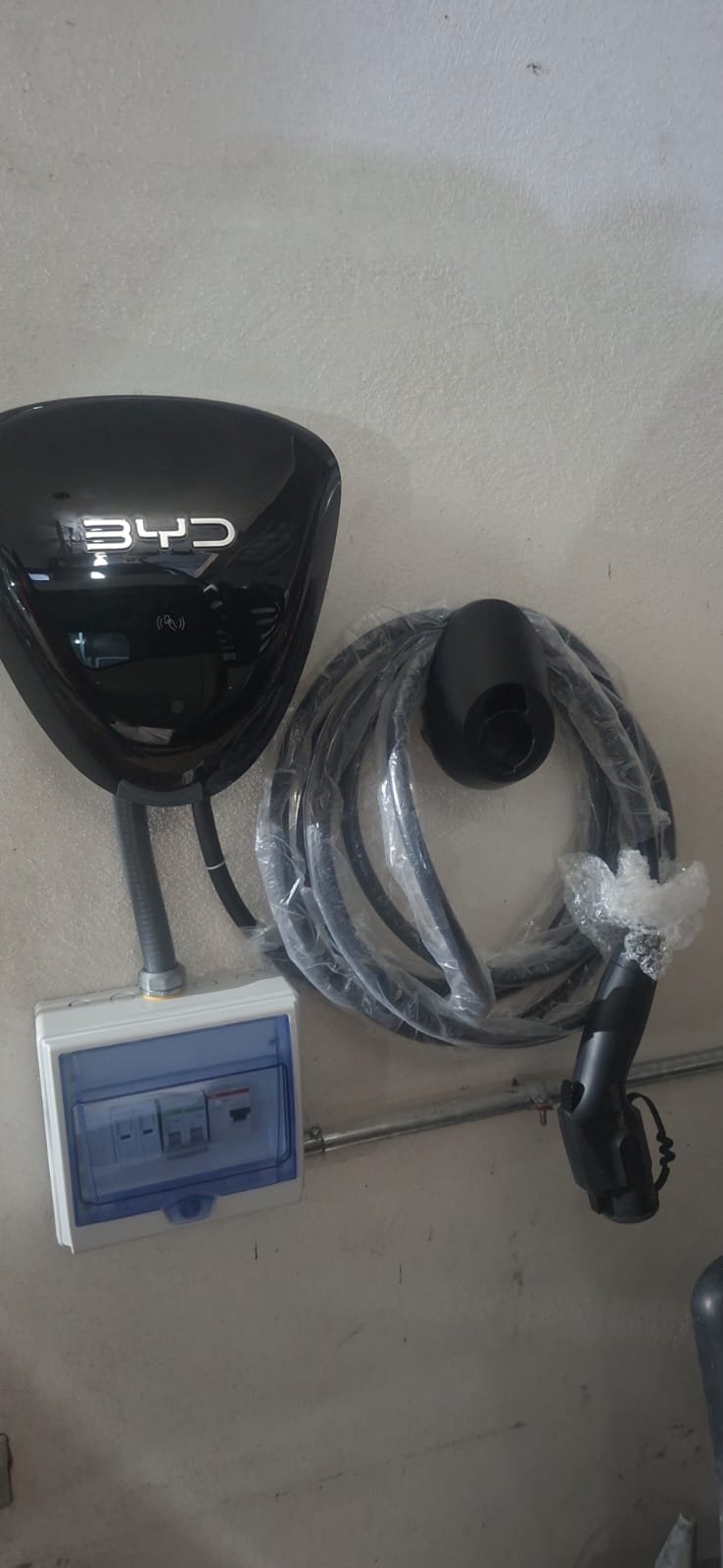 Lavadora eléctrica de color negro con cable enrollado y caja de distribución eléctrica en la pared.
