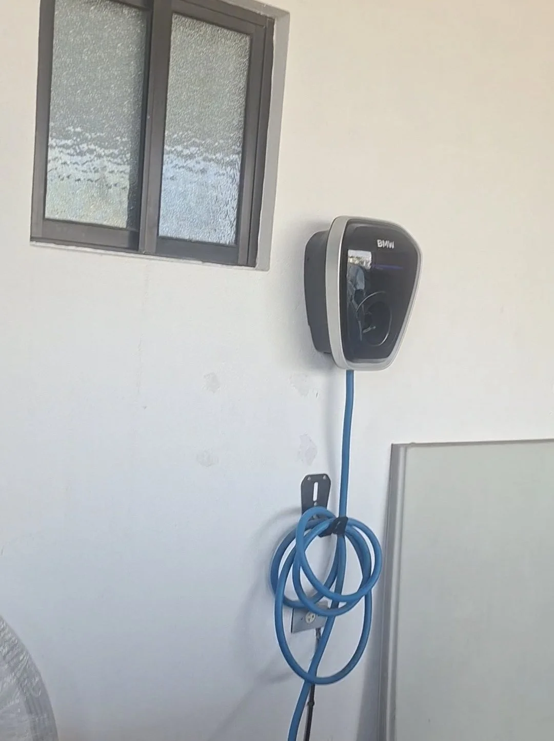 Cargador de coche eléctrico BMW en una pared blanca junto a un cable azul enrollado.