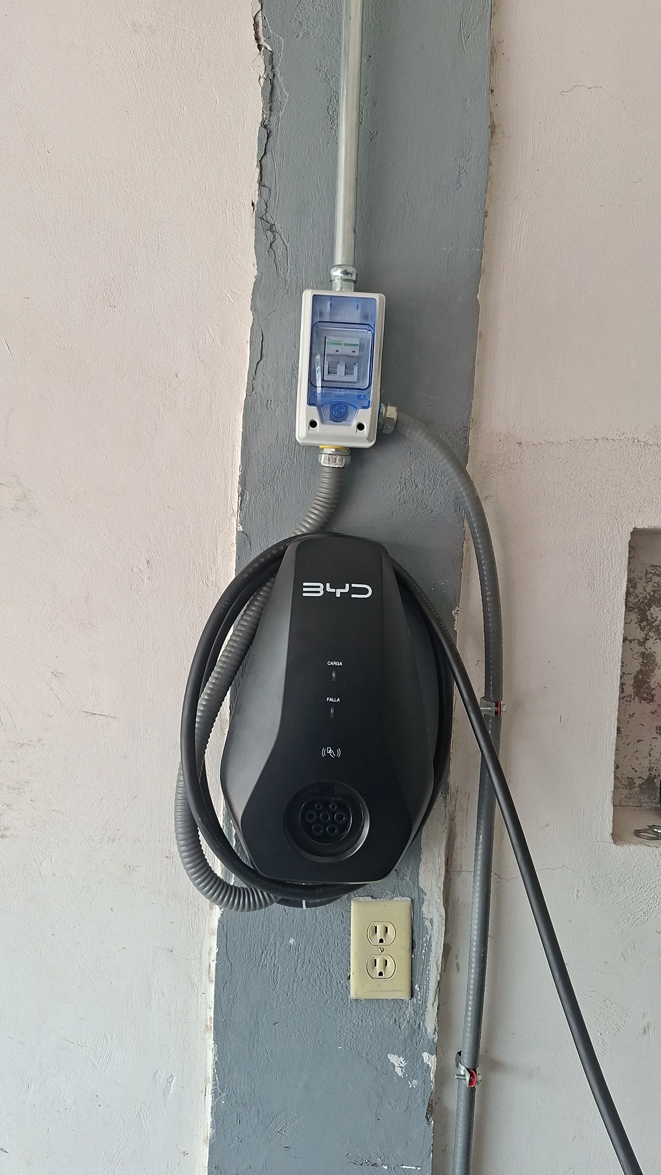 Sistema de carga de coche eléctrico en la pared, con cables conectados, enchufe y caja de control, en un espacio interior.