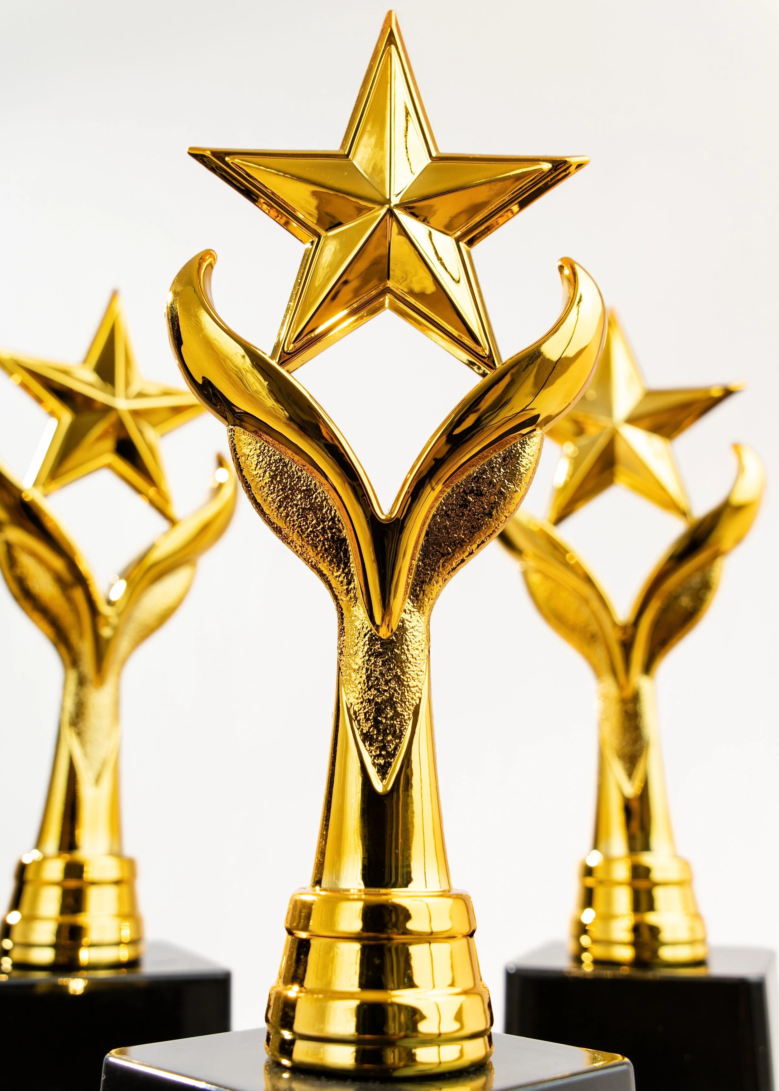 Golden star-shaped trophies with a three-dimensional design, mounted on black bases, displayed against a plain white background.