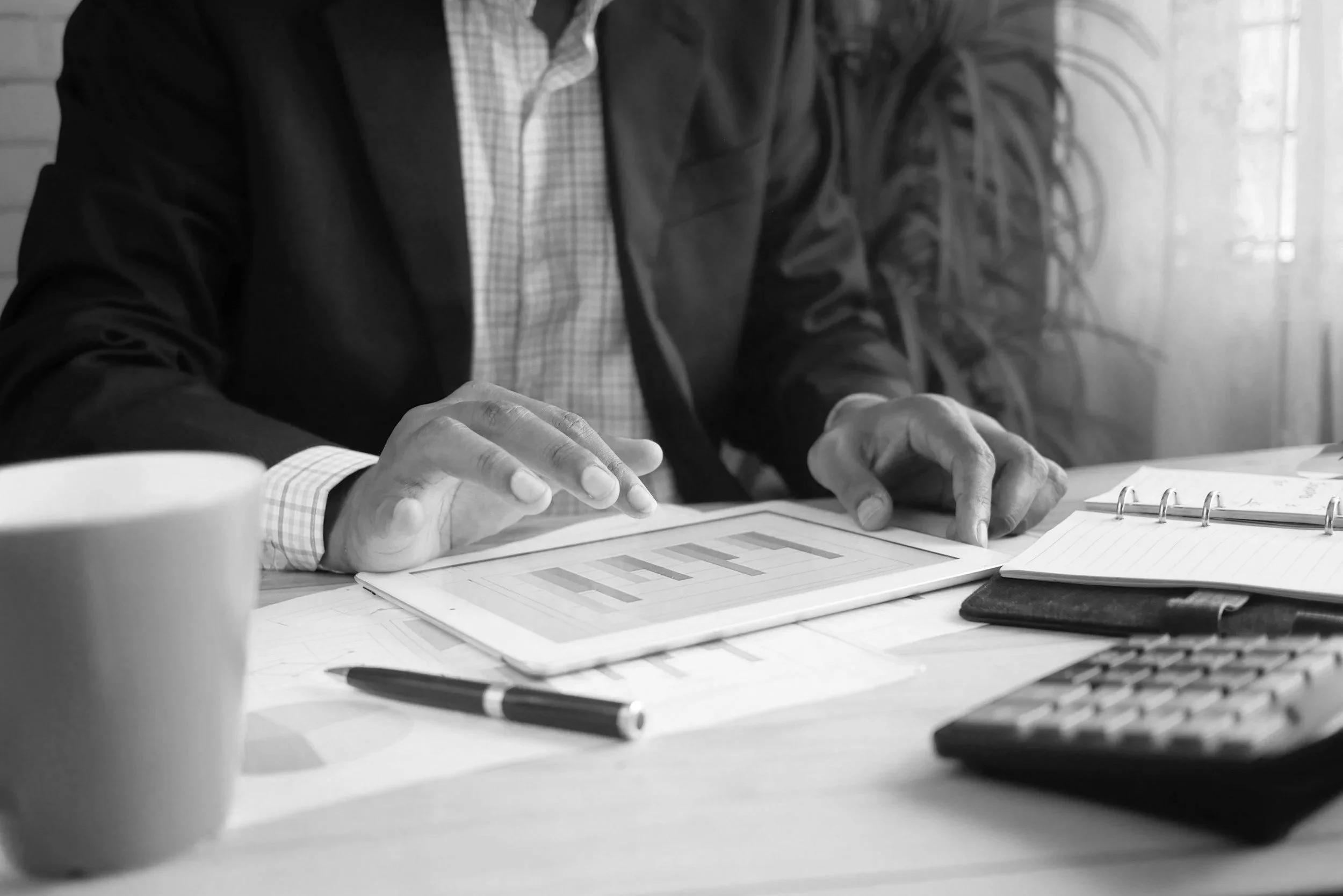 Close-up of a man in a suit and a woman with long hair sitting at a desk, reviewing a printed chart or spreadsheet with a pen and notebook nearby.