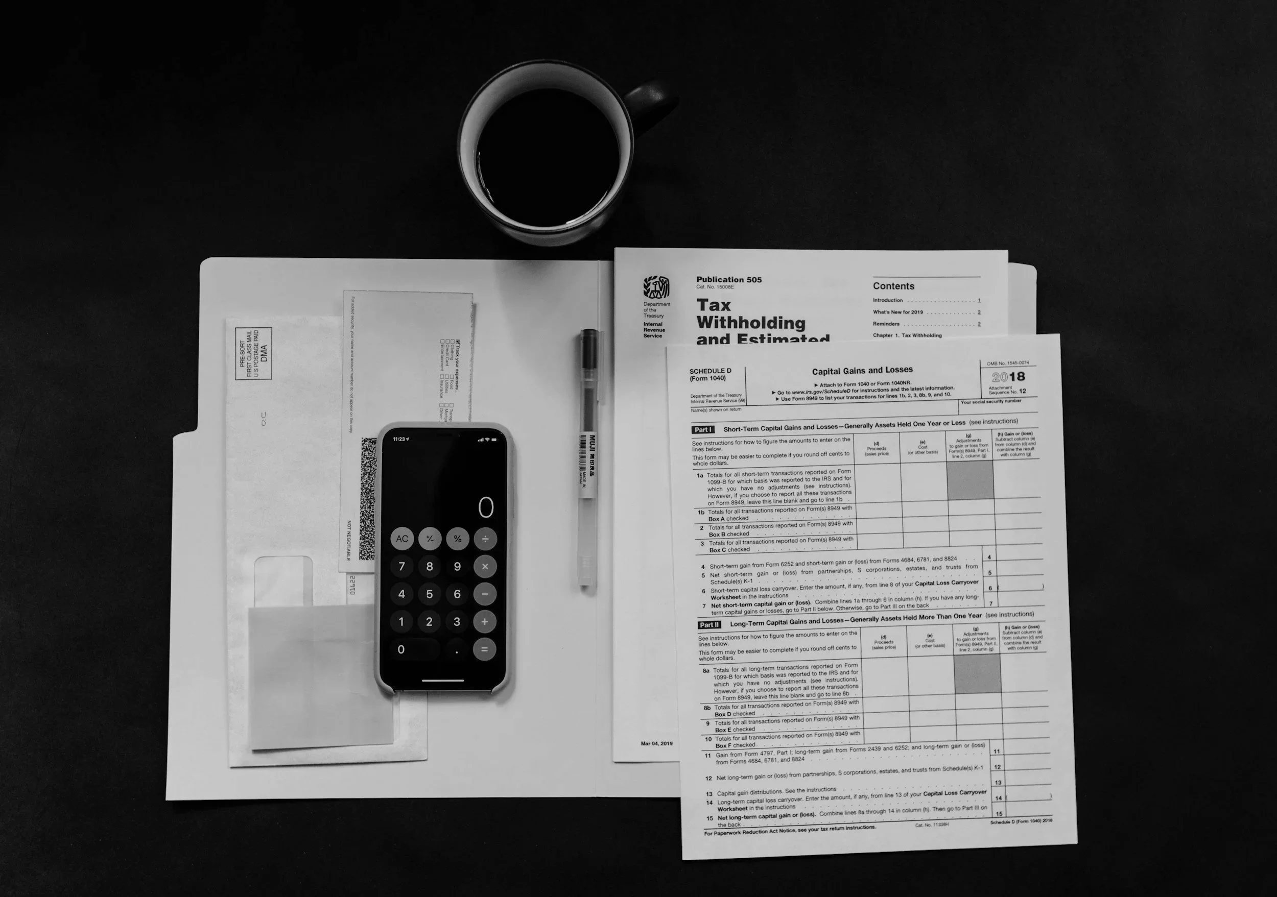 Overhead view of a workspace with a cup of black coffee, an open tax document, a calculator, a pen, and a smartphone on a dark surface.