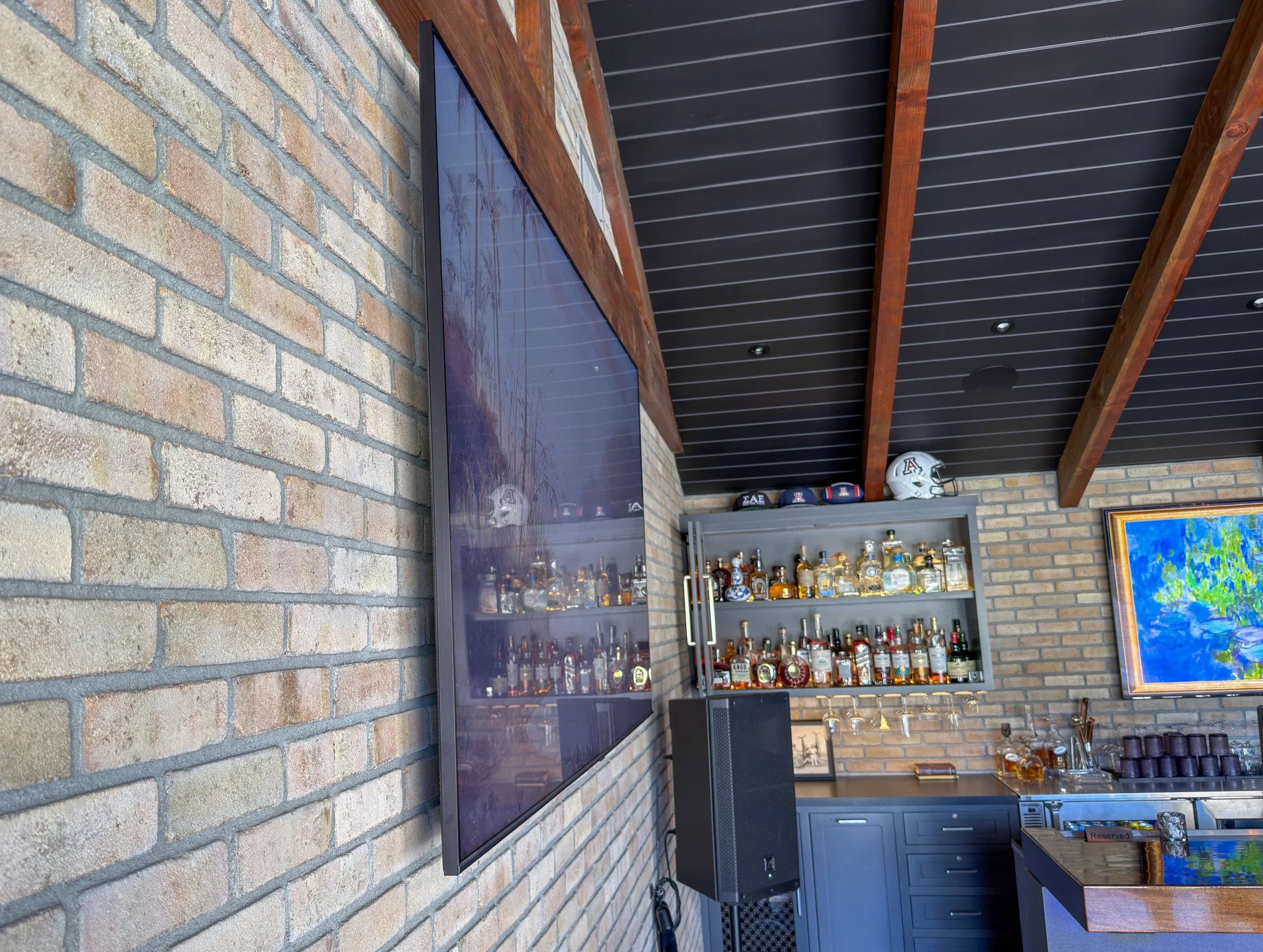 a thin LED screen mountain on a brick wall with a liquor cabinet in the background.