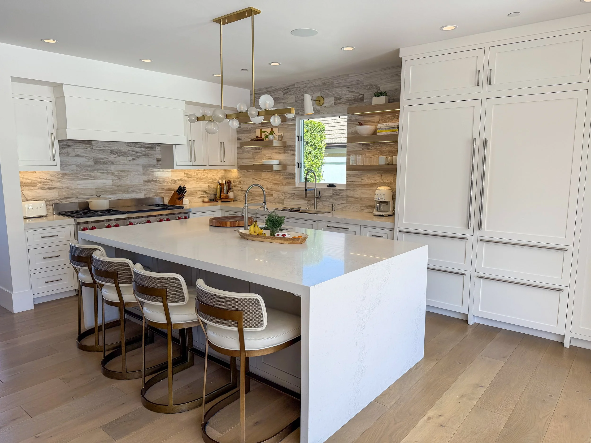 Modern kitchen with white cabinets, a large center island, a marble backsplash, floating shelves, and a unique gold and globe chandelier overhead.