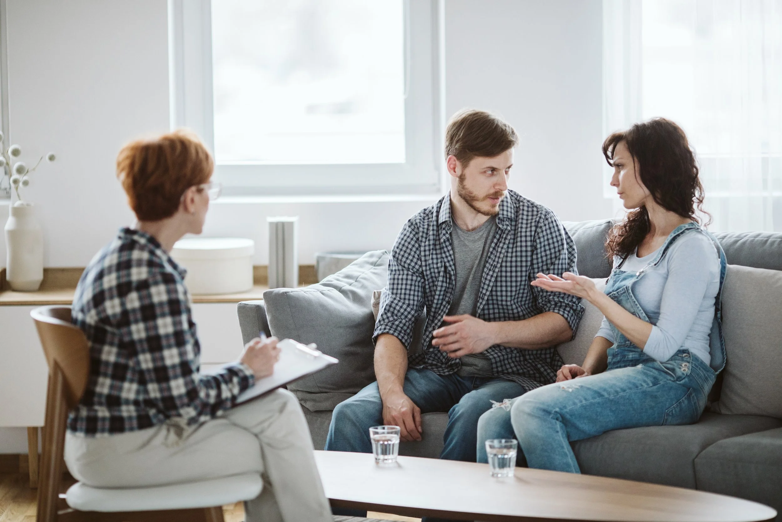 A group therapy session with a therapist taking notes and three patients engaging in discussion in a bright, modern room.