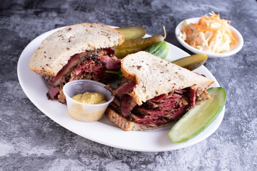 Reuben sandwich with sliced corned beef, sauerkraut, and Swiss cheese on rye bread, served with pickles, mustard, and coleslaw.