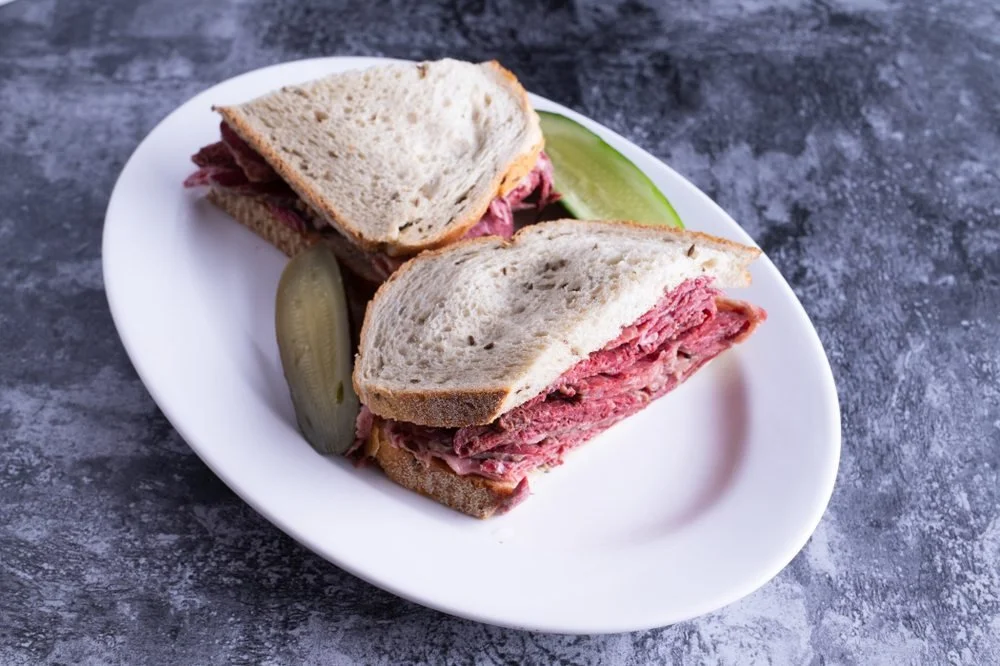 Roast beef sandwich with sliced pickles on a white plate.