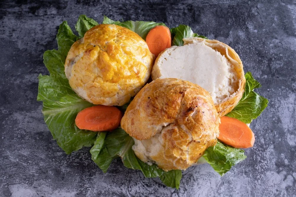 Biscuits with cheddar cheese, one halved to show a creamy filling, garnished with lettuce and carrot slices on a dark surface.
