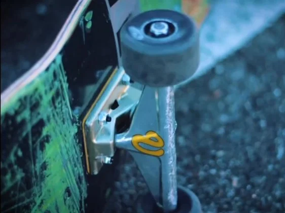 Close-up of a skateboard's metal truck and wheel on an asphalt surface with visible motion blur.