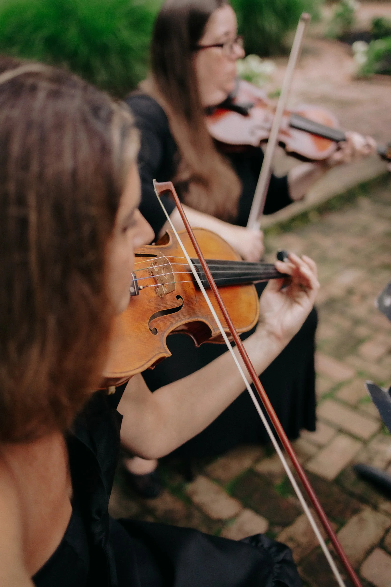 People playing violins outdoors in a group setting.