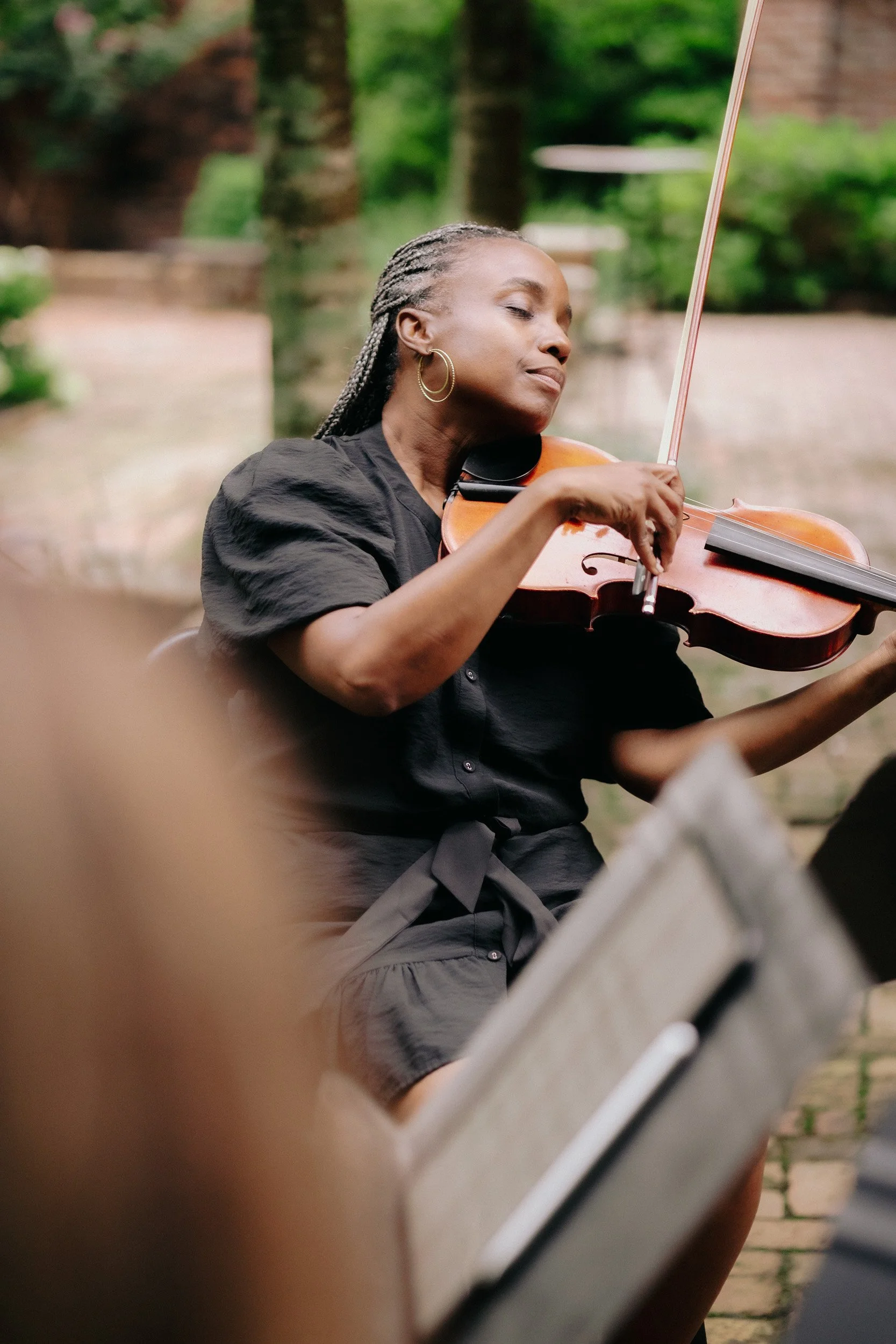 Woman with braided hair and hoop earrings playing a violin outdoors.