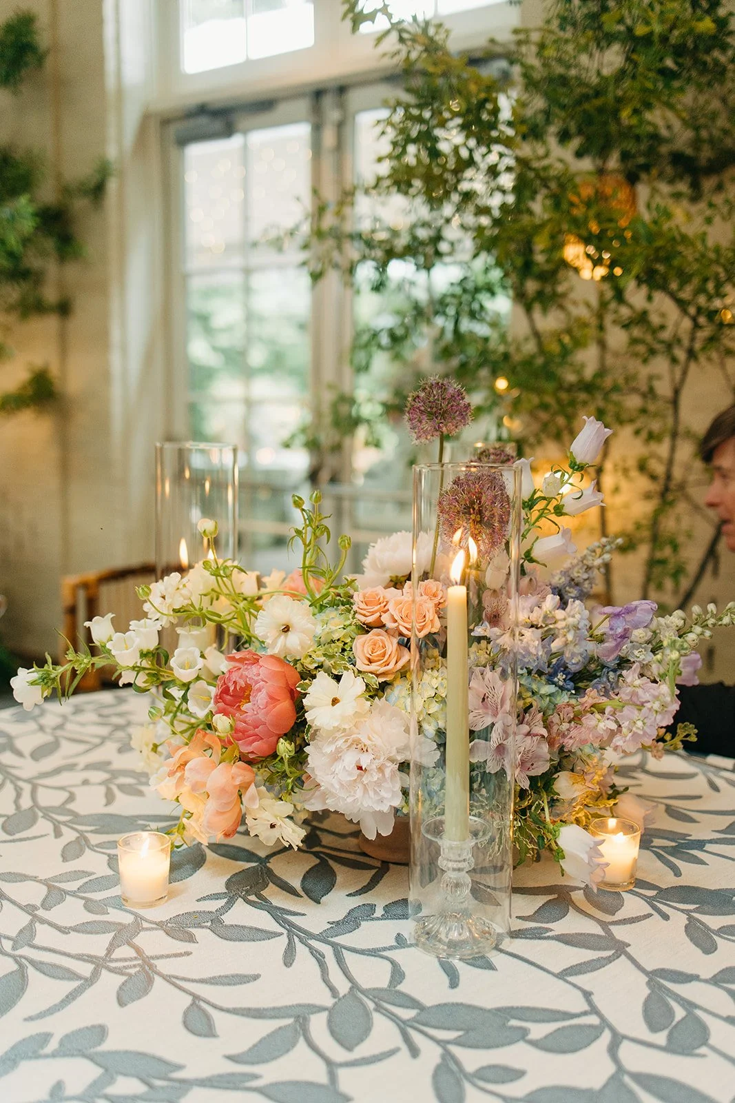 Elegant floral centerpiece with candles on a decorated table at a bright indoor event space.