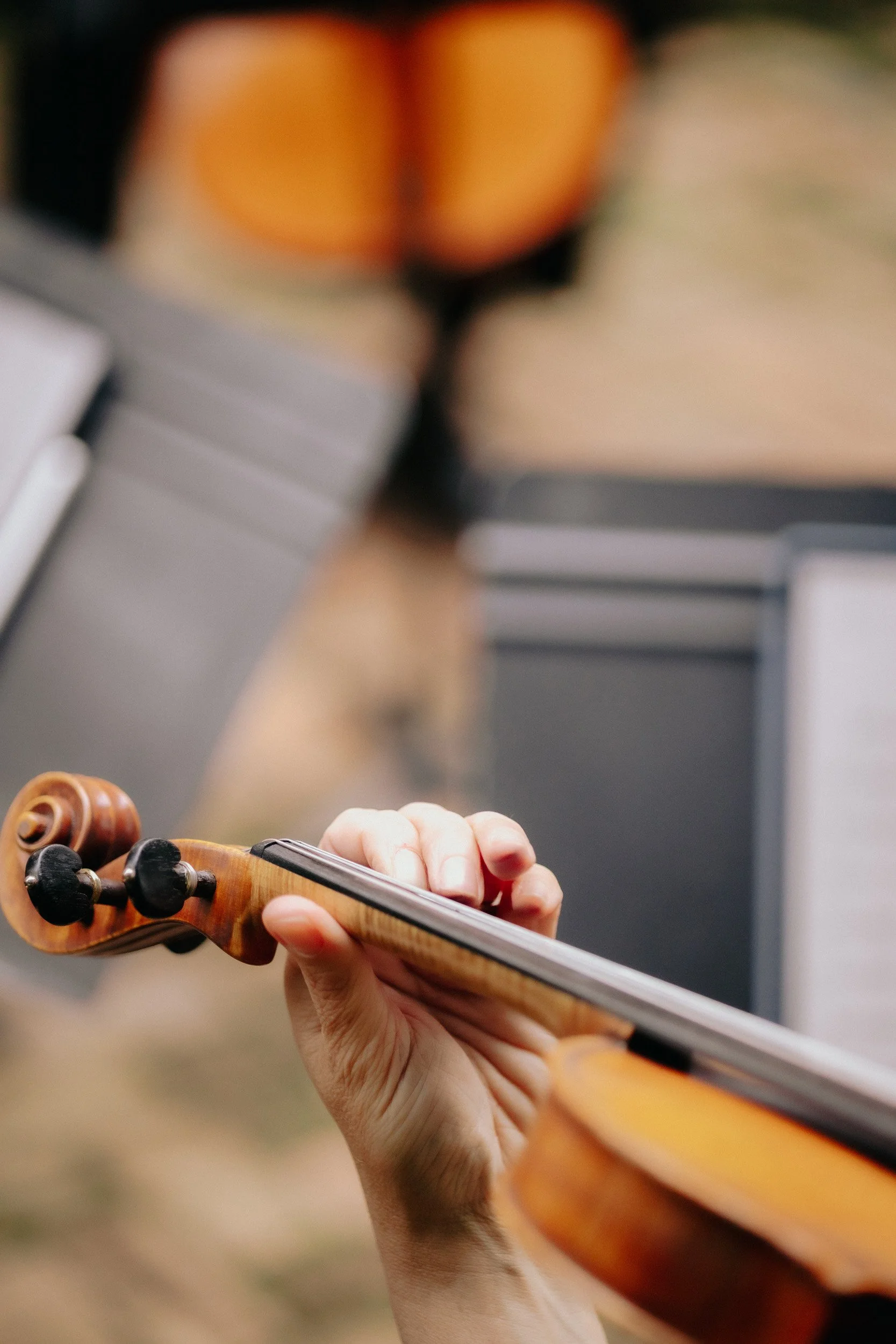 Close-up of a person playing a violin, focusing on their hand and the scroll of the violin.