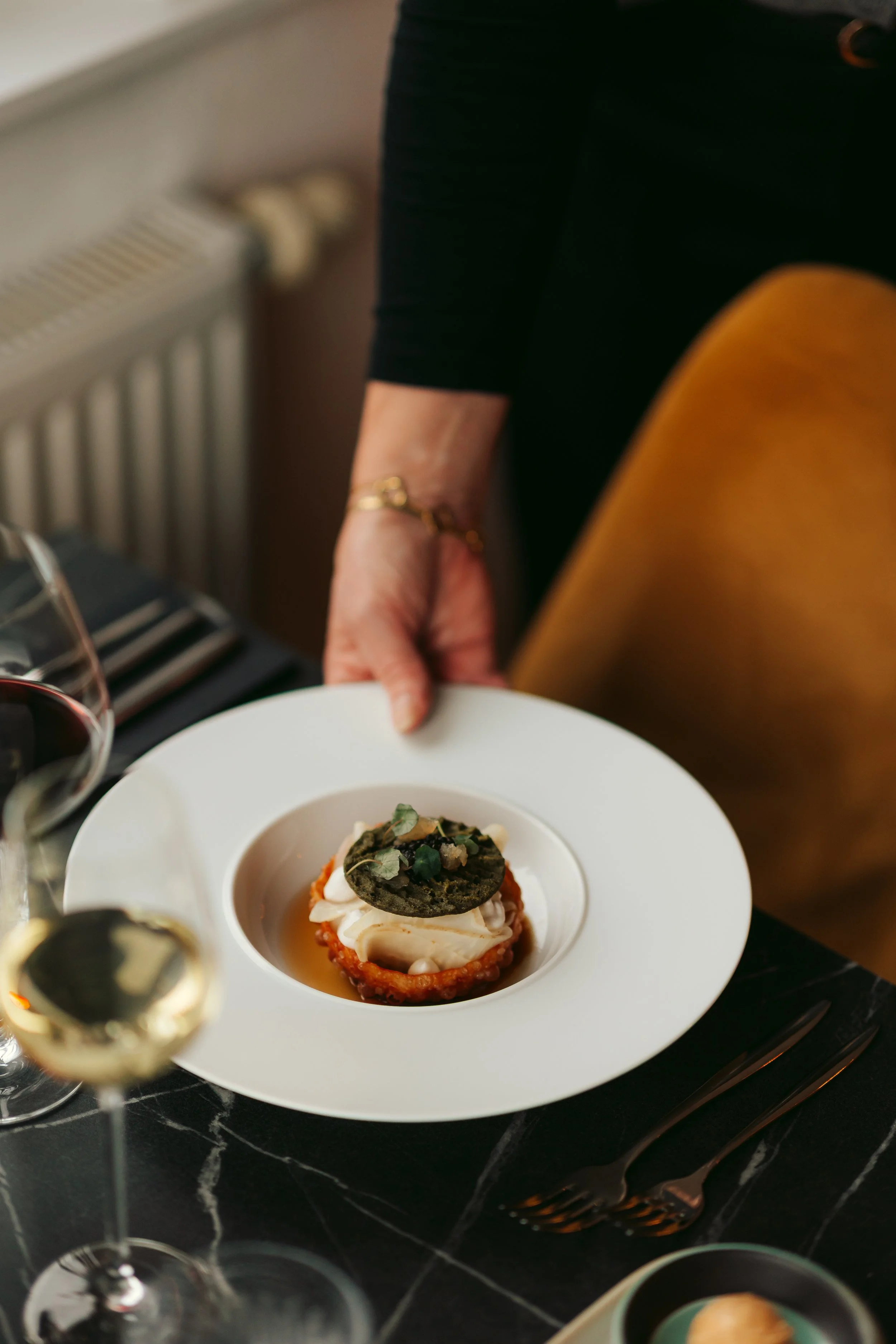 Els die een bord serveert met een vegetarisch voorgerecht met tomaat, geitenkaas en een krokantje