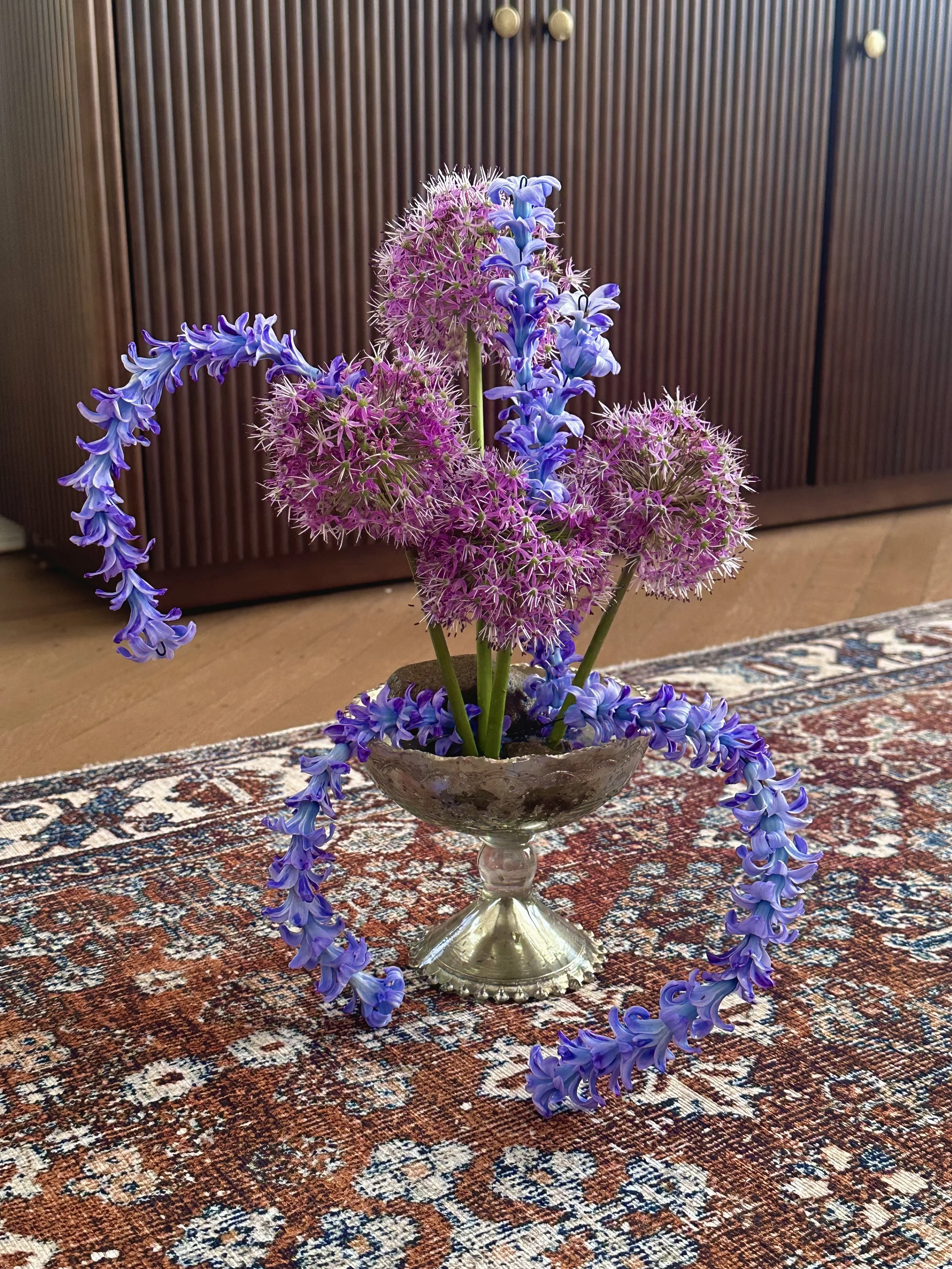 A floral arrangement with blue and pink flowers in a glass bowl on a patterned rug.