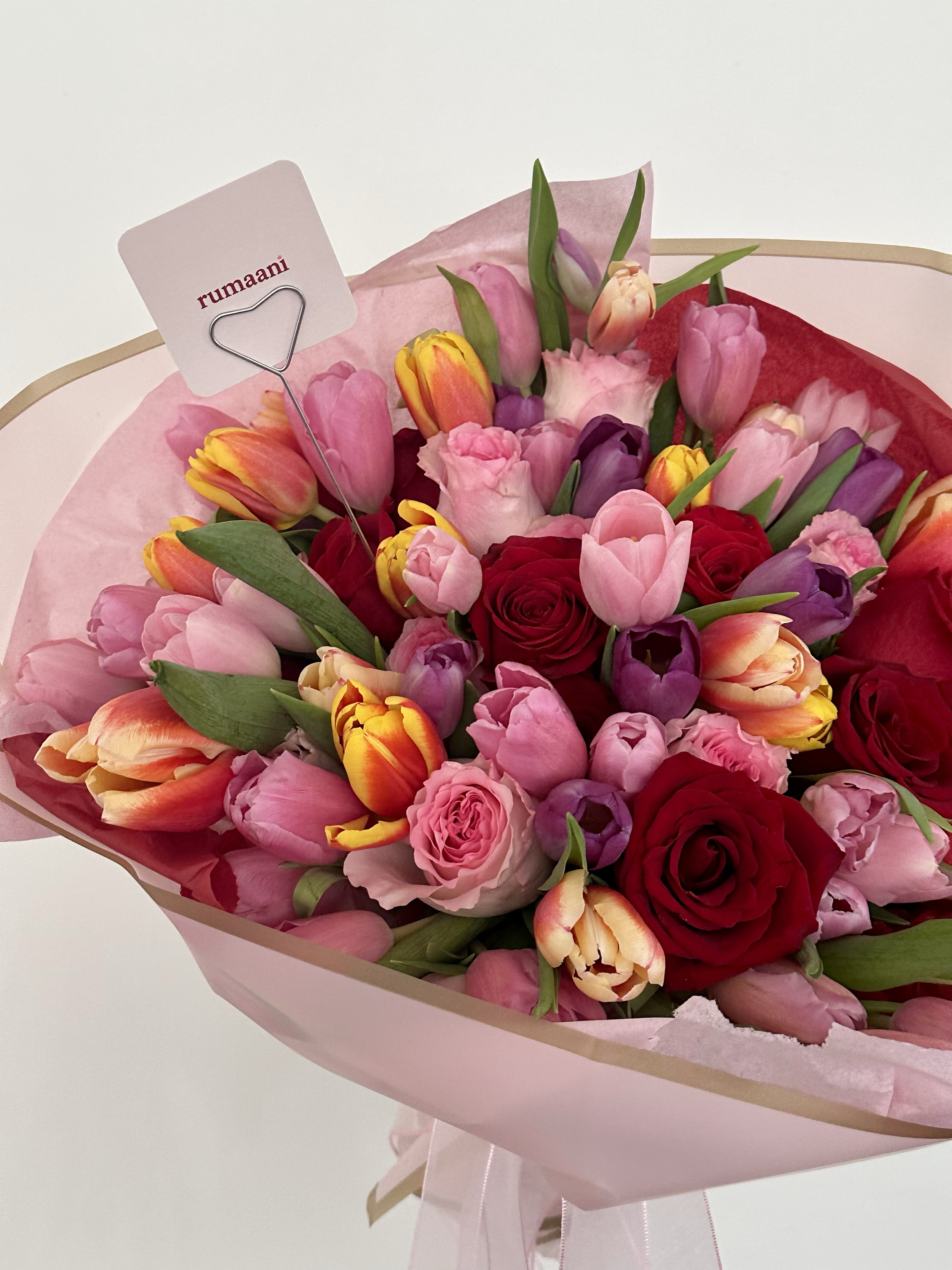 A bouquet of various pink, purple, yellow, orange, and red flowers wrapped in pink paper with a ribbon.