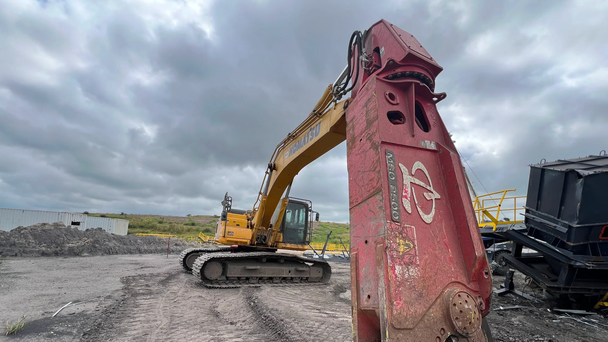 A large yellow and black excavator at a construction site with a cloudy sky overhead.