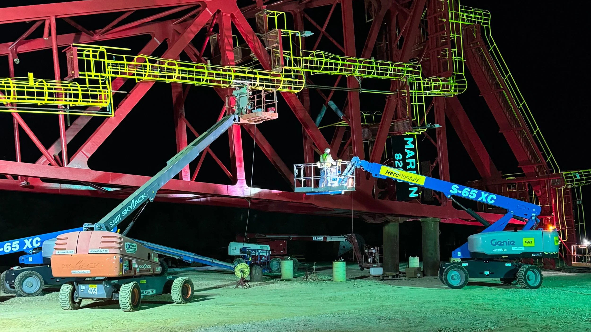 Workers on lifts inspecting a large structure at night.