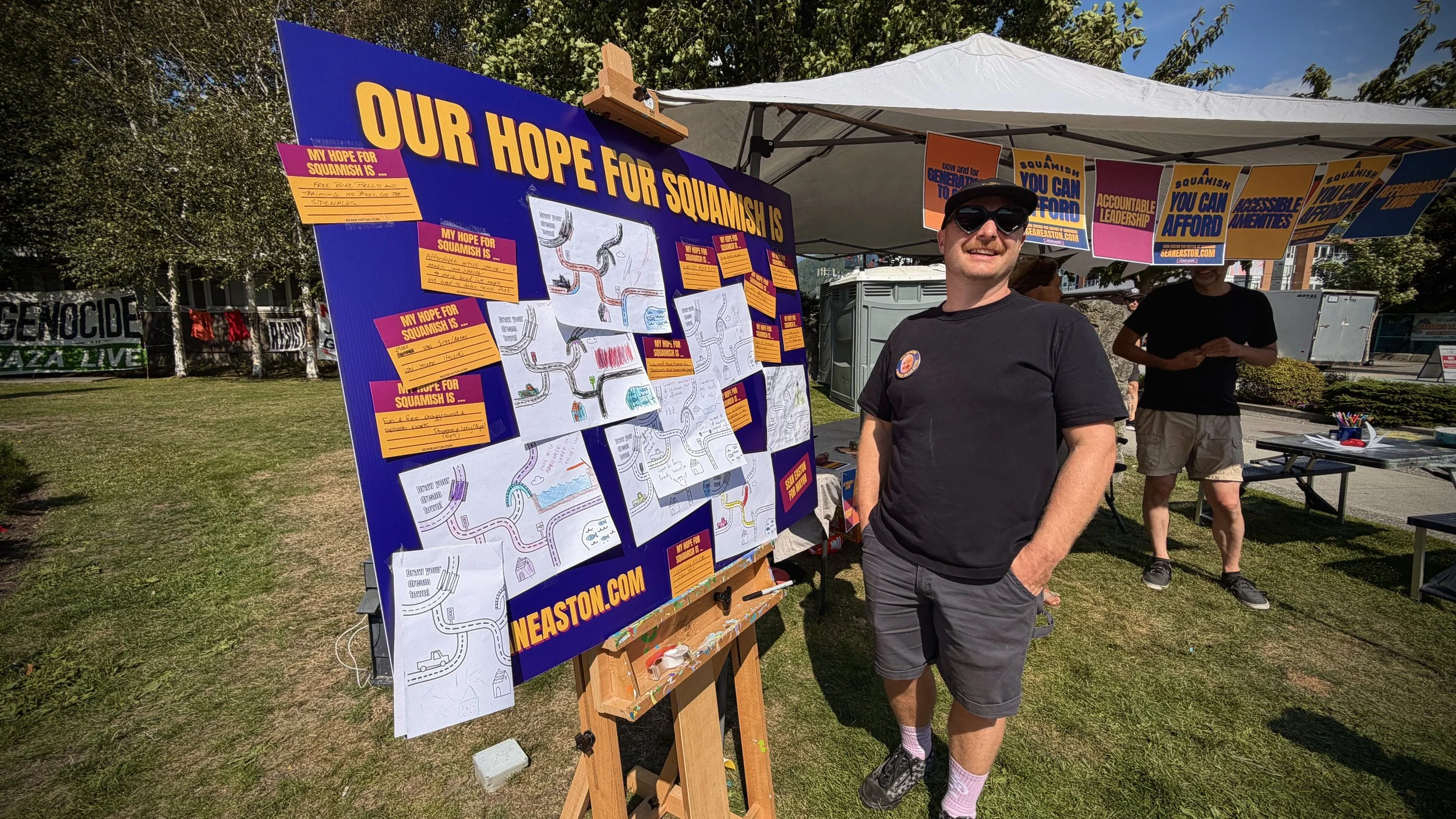 A photograph of Sean at a local park standing with a community board filled with ideas of residents' hopes for Squamish