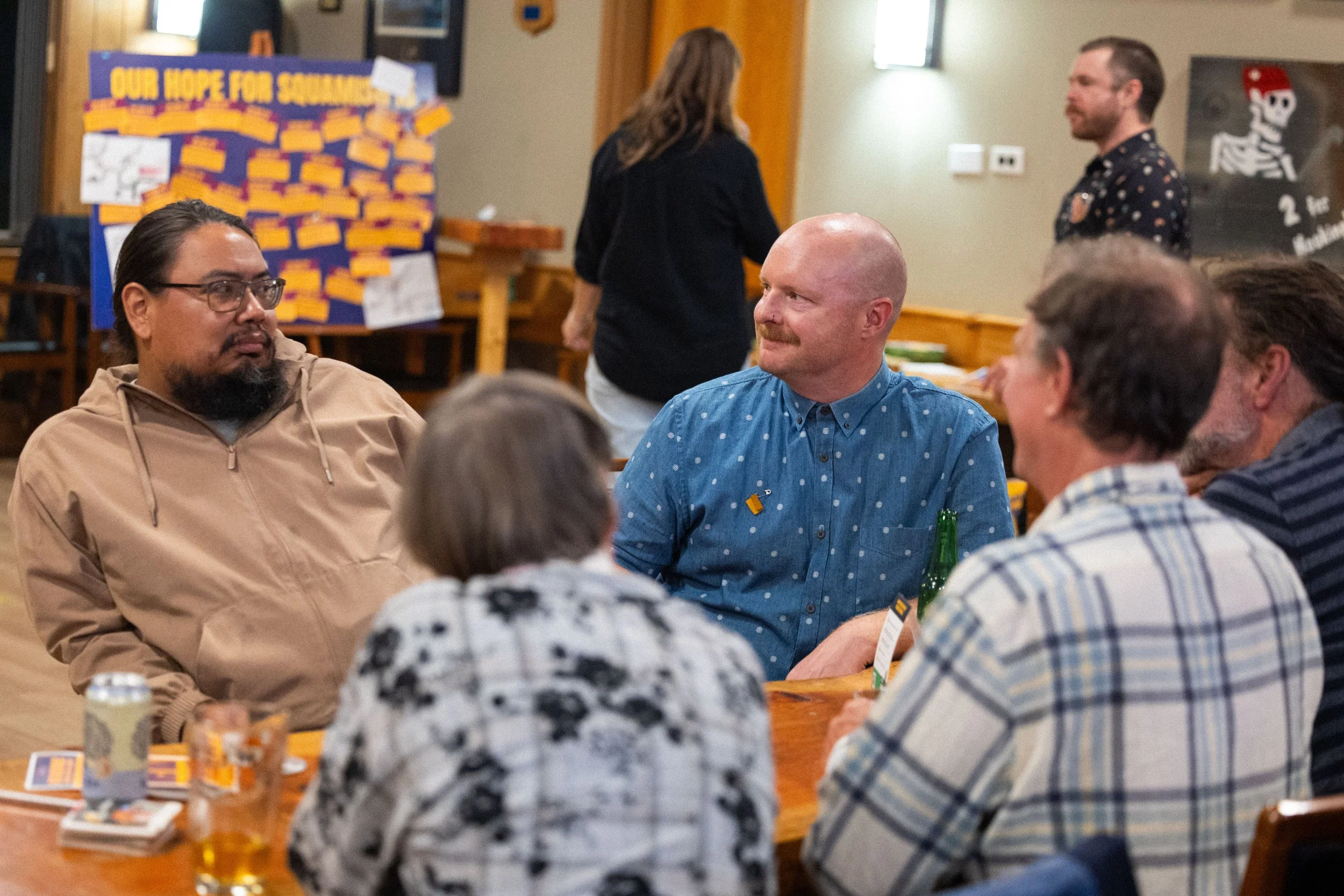 A photograph of Sean sitting at a table with three other people. They are deep in conversation, focused on listening to one man.