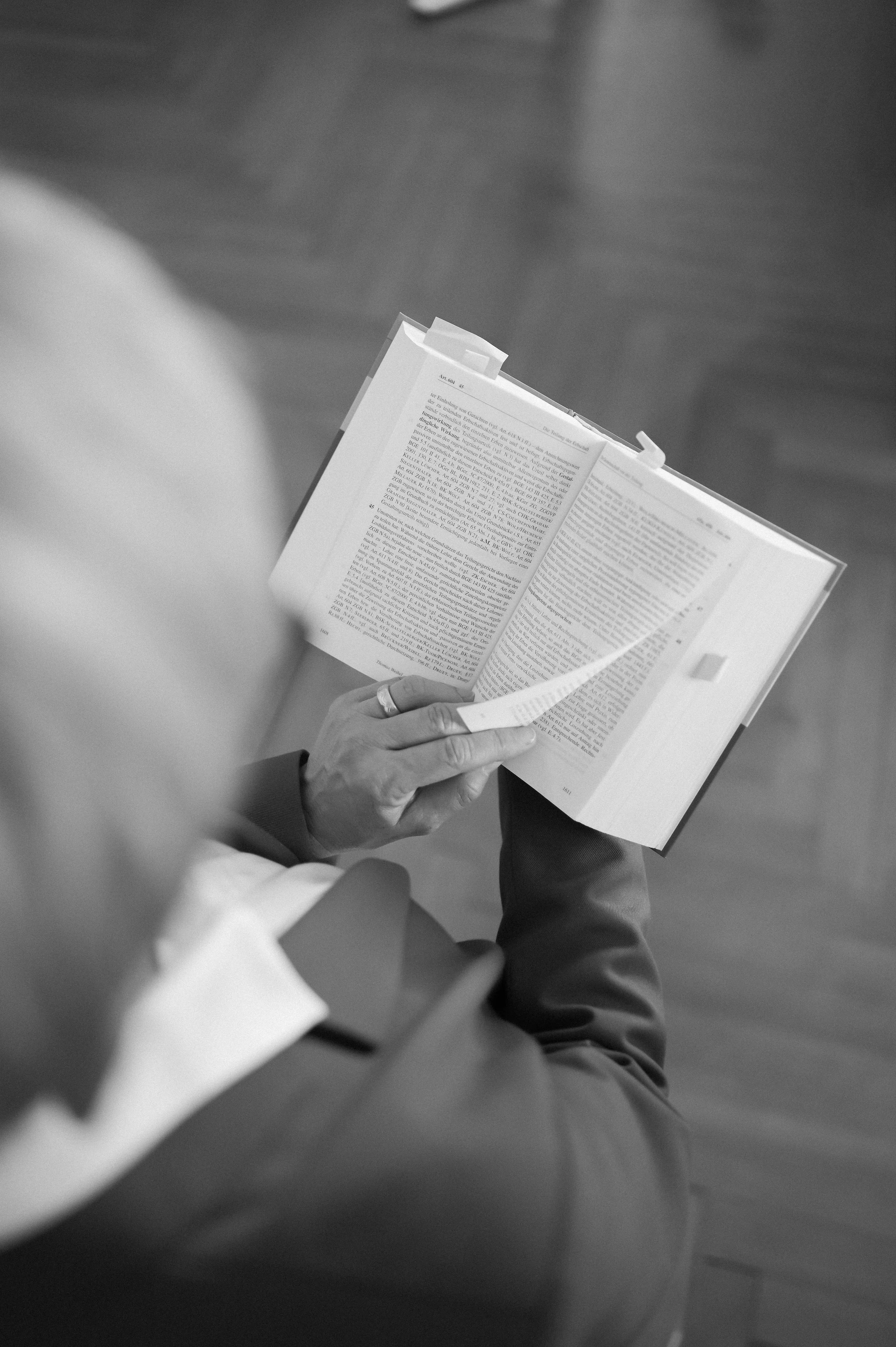 Eine Person liest ein offenes Buch, gesehen aus einer seitlichen Perspektive, auf einem Holzfußboden.