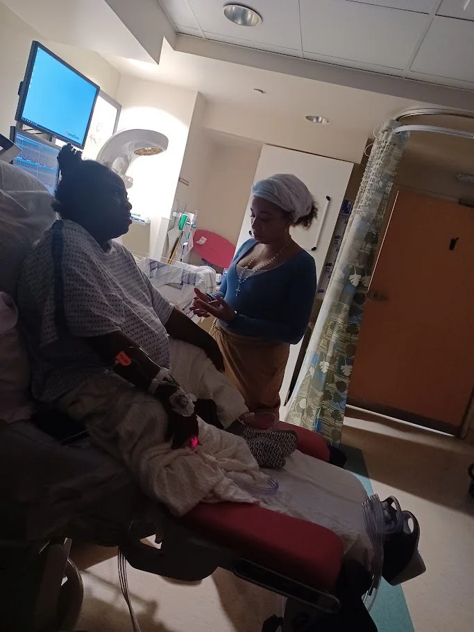 A patient lying in a hospital bed talking with a woman standing beside the bed