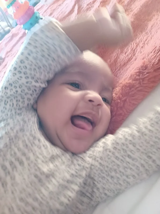 A smiling baby lying on a soft blanket, with a pacifier and a plush toy nearby.