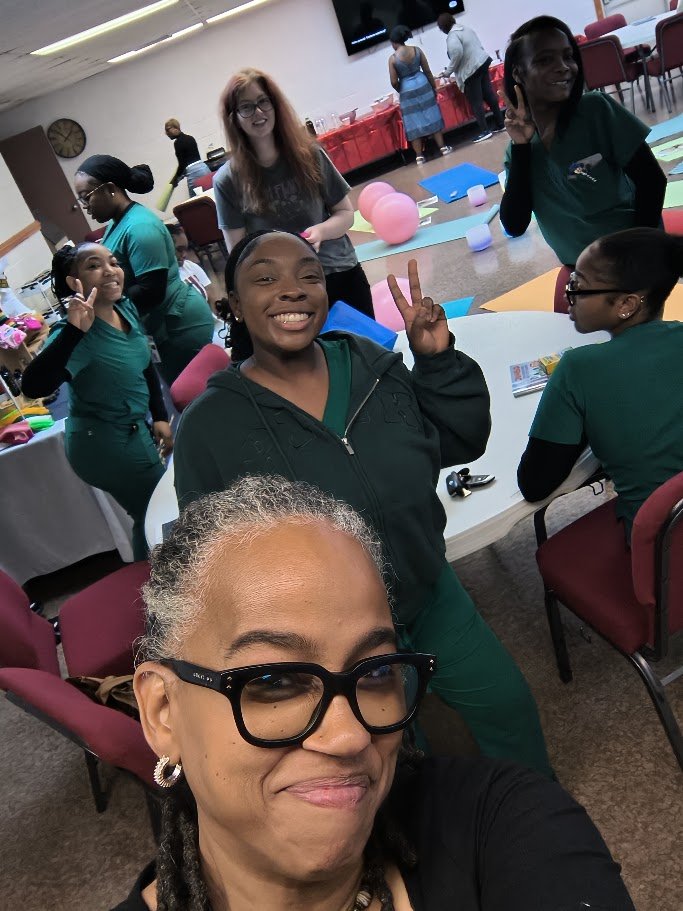 Group of women smiling and posing for a selfie at a celebration or event, with colorful decorations and tables in the background.