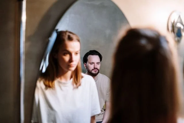 woman looking in mirror with man looking over her shoulder