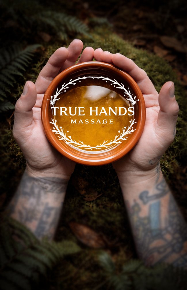 Hands with tattoos holding a small pottery bowl with a beverage, resting on mossy ground and ferns outdoors. True Hands Massage Business Card.