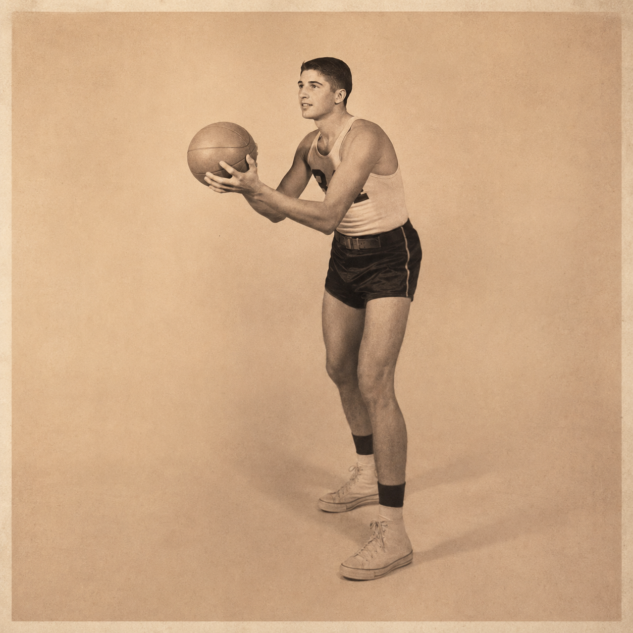 A young man in a vintage athletic uniform holding a basketball, standing in a ready position, against a plain background.