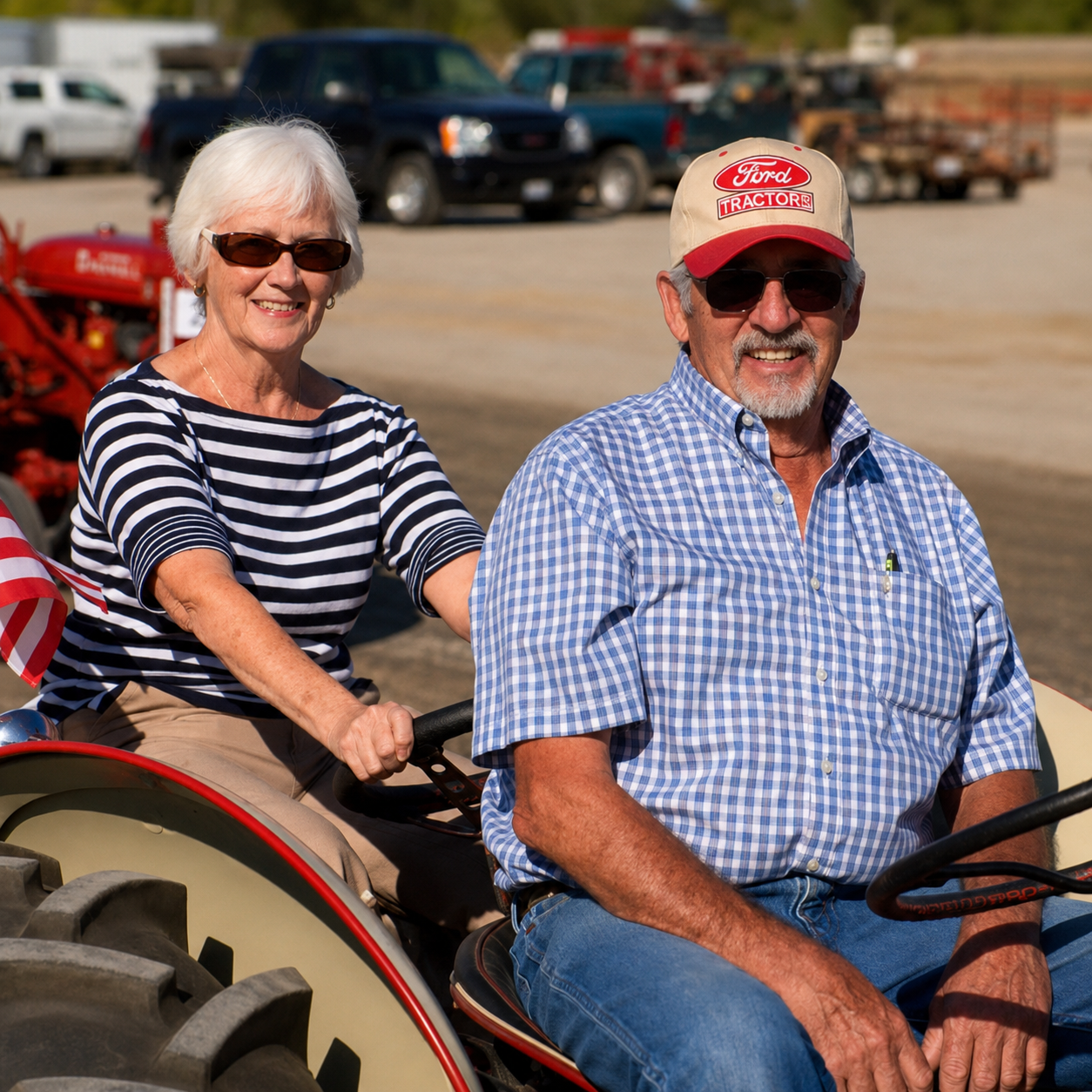 An elderly woman and man riding a tractor outdoors. The woman is smiling and wearing a striped shirt and sunglasses, while the man is also smiling, wearing sunglasses and a checkered shirt with a Ford Tractor cap.