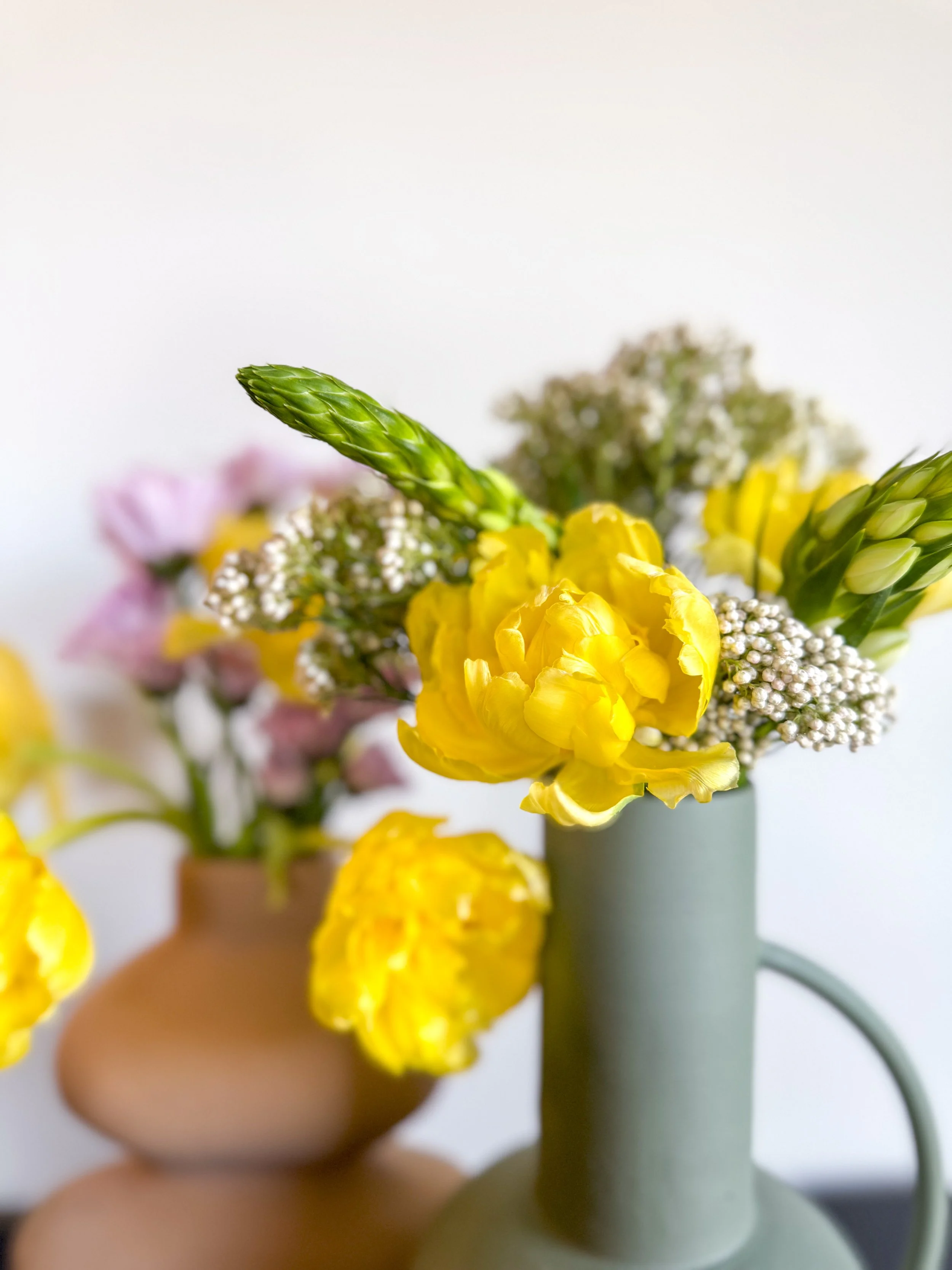Close-up of a yellow flower in a vase, with greenery, in a minimalist setting.