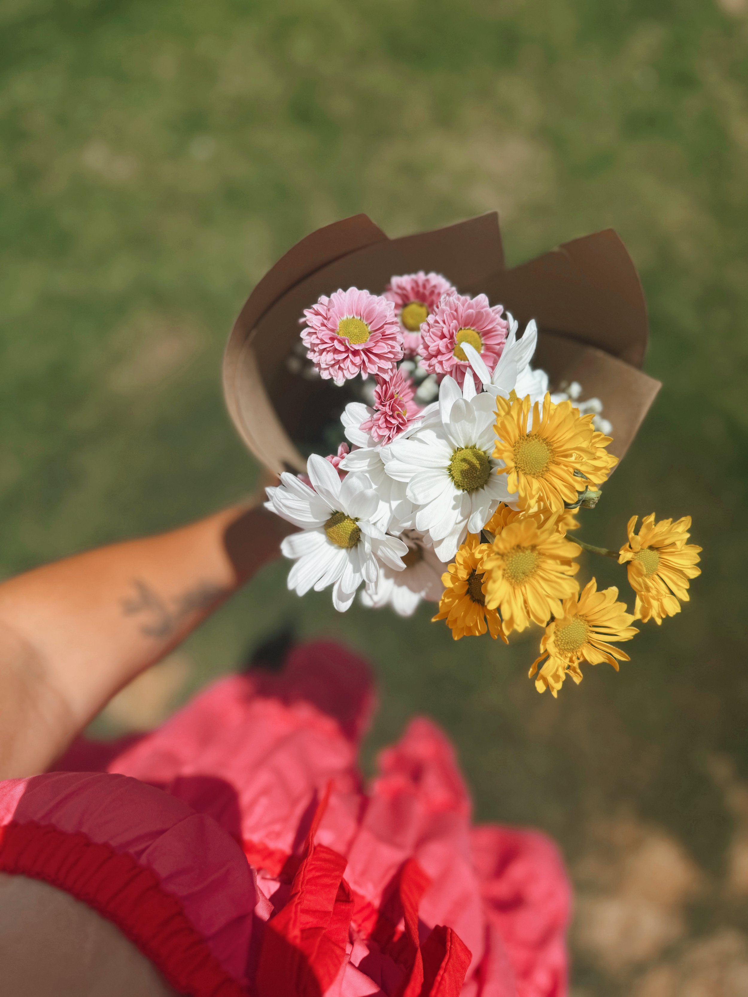 A hand holding a bouquet of pink, white, and yellow flowers with a blurred background.