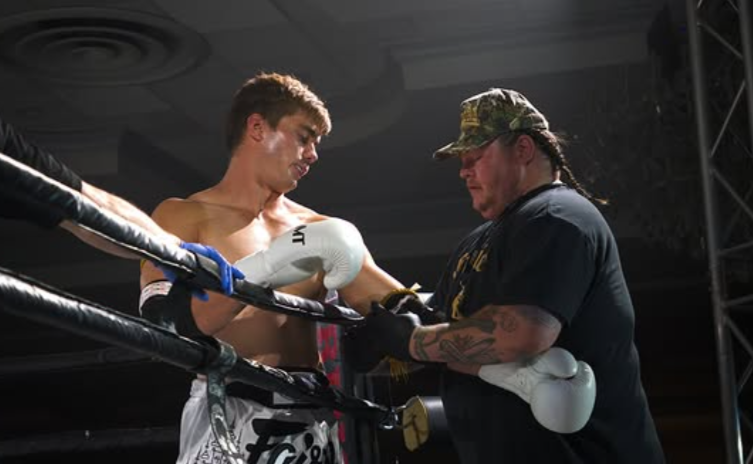 Boxer in white gloves getting assistance from a trainer in a boxing ring.