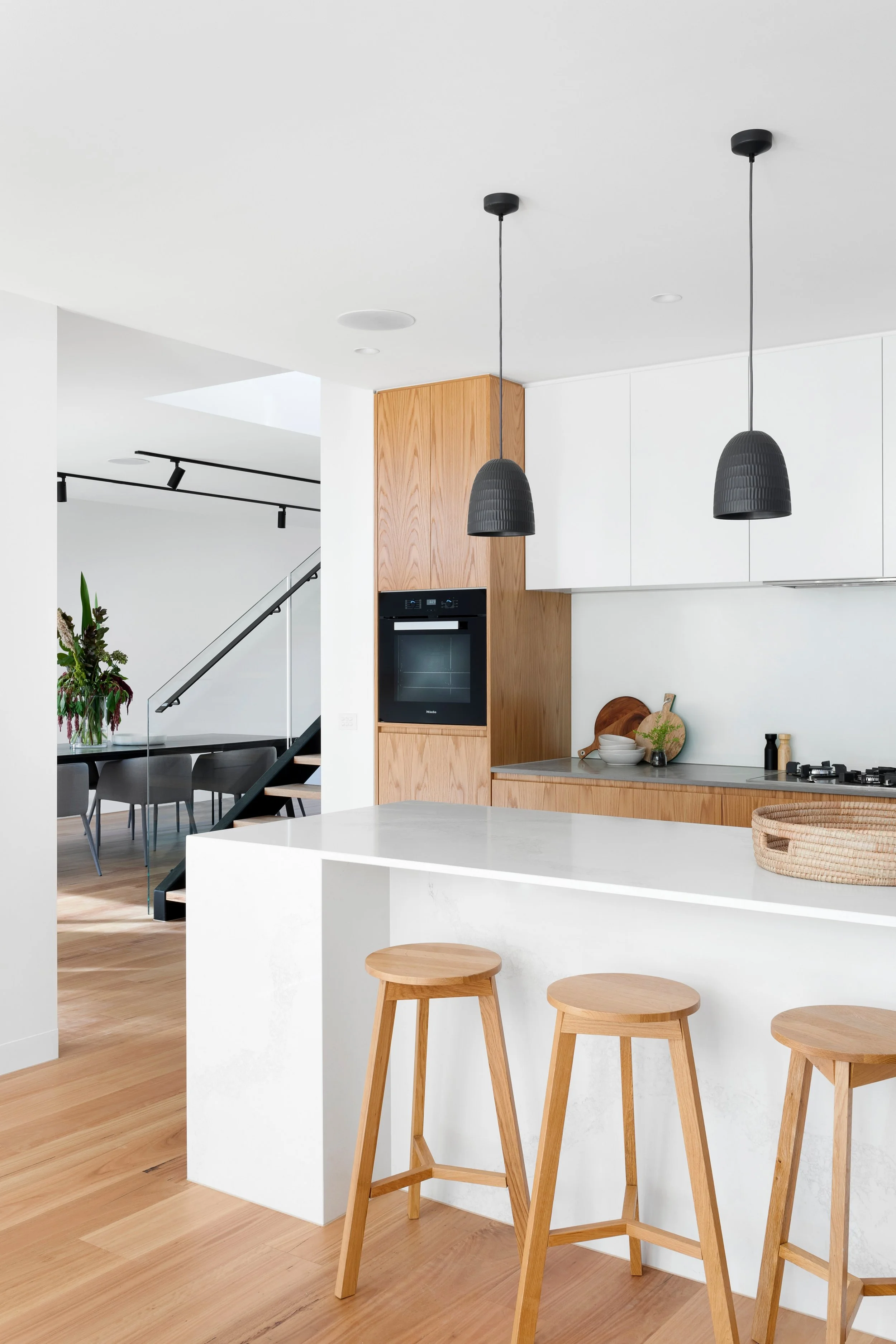 A modern kitchen with a white island, three wooden bar stools, black pendant lights, and white cabinets.