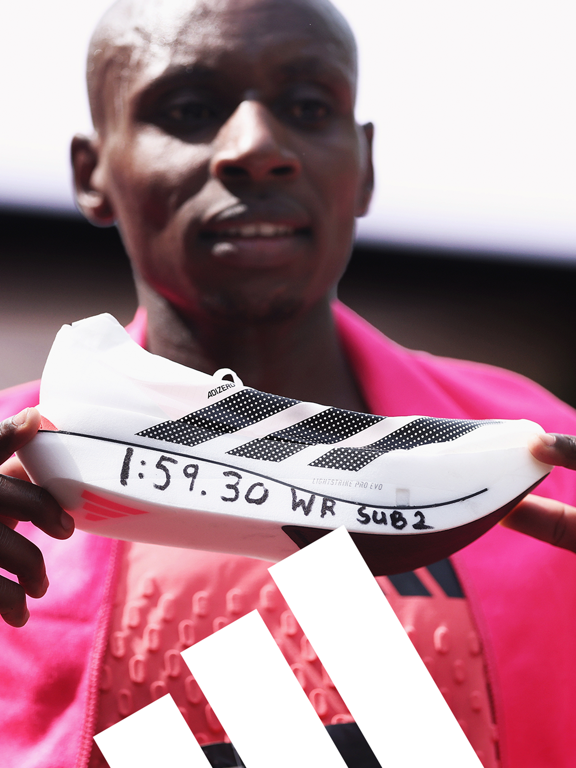 Close-up of a person holding an athletic shoe with a race bib on it, wearing a pink athletic jacket. The race bib has handwritten time and event details.