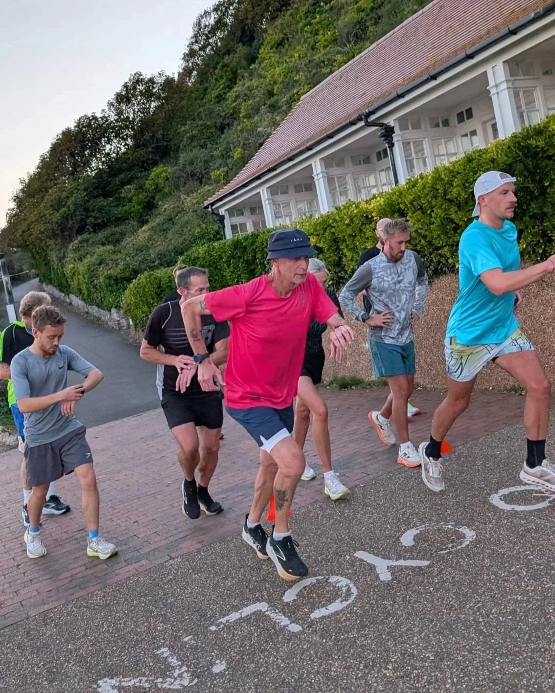 A group of runners participating in a park or street race, with some looking at their watches as they start running.