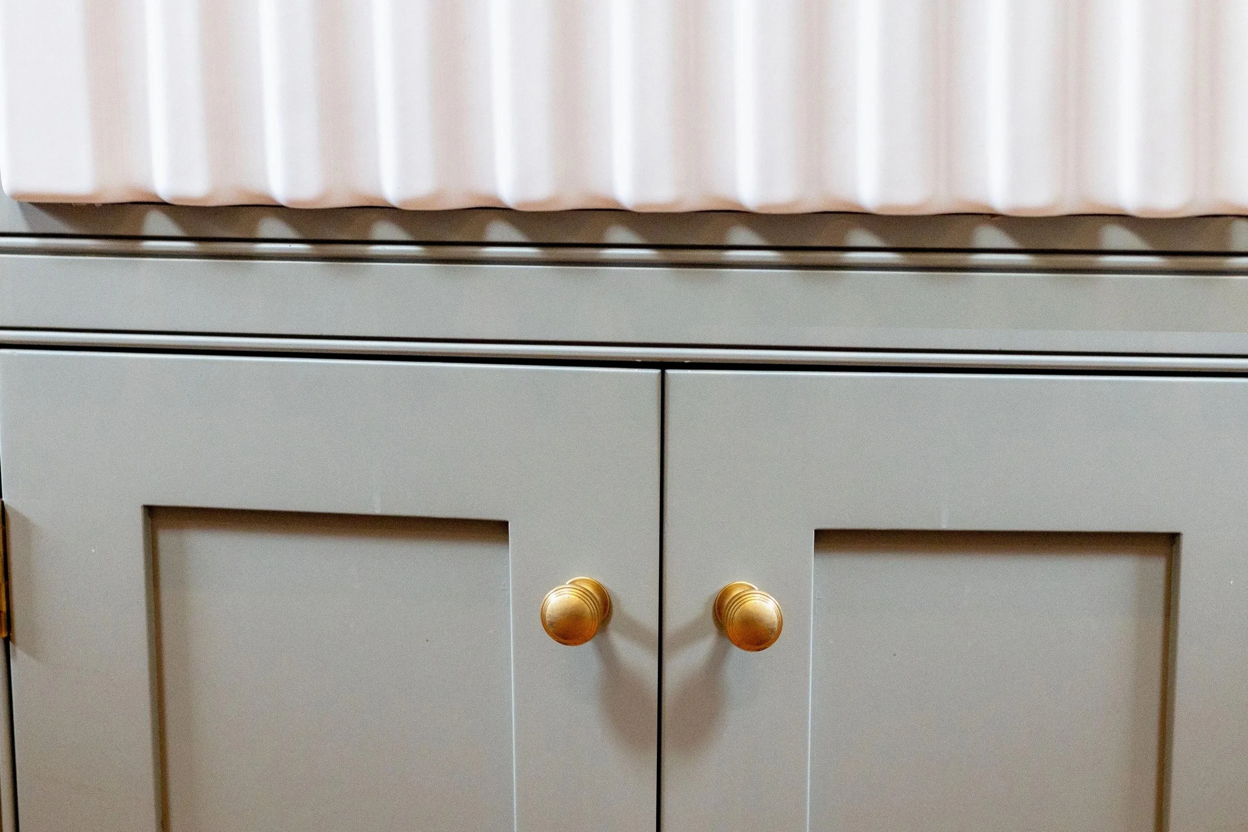 Close up of a green sage handmade kitchen unit with brass handles..