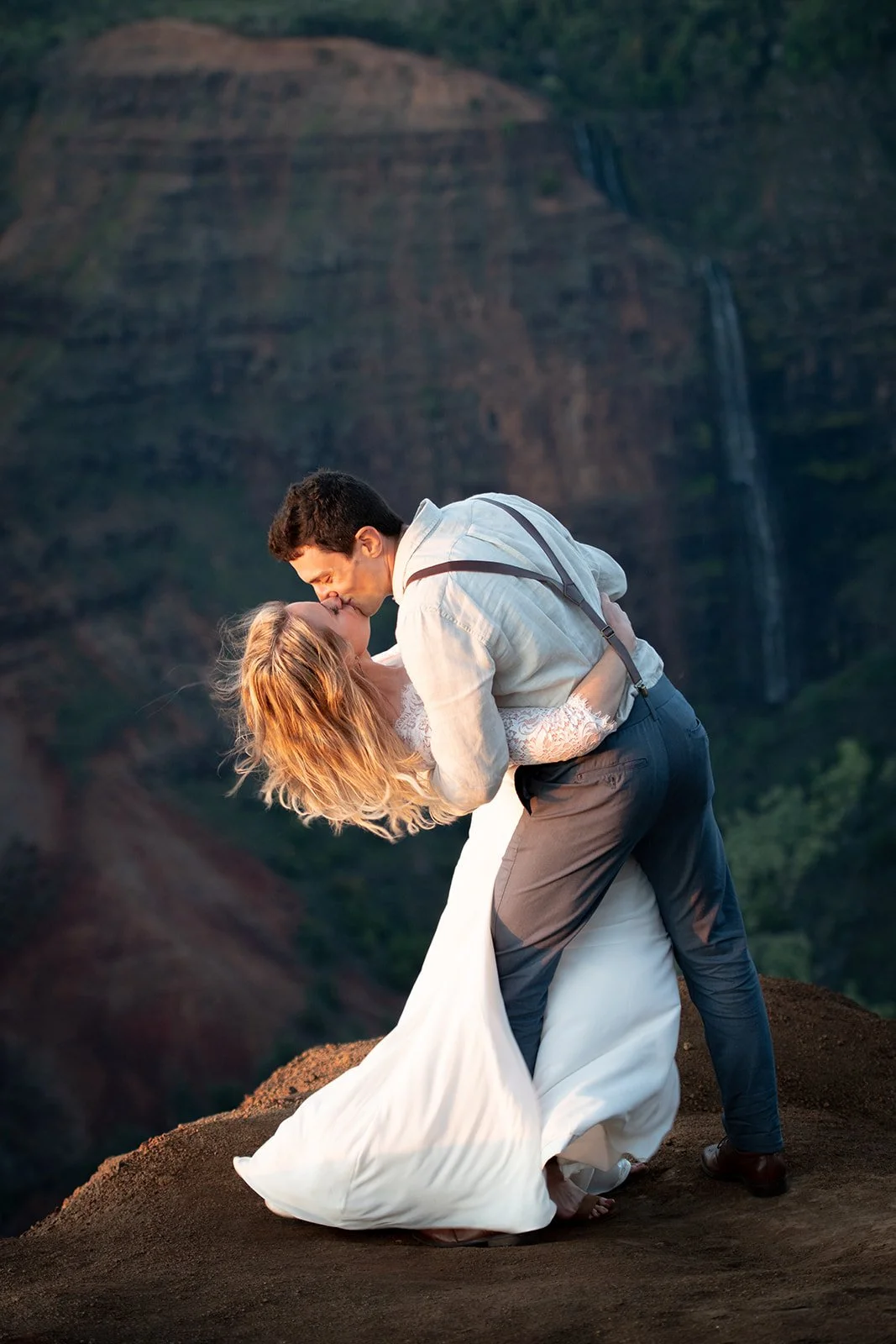A couple kisses after they elope in Kauai Hawaii on a mountain in front of a waterfall