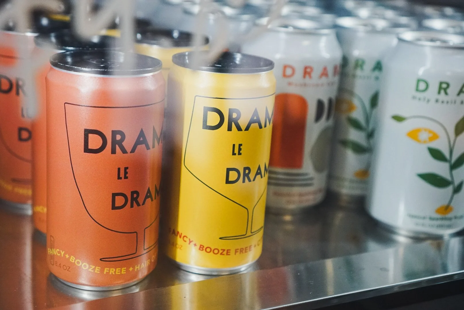 Cans of drunk le drunk non-alcoholic beverage on a store shelf, with some cans featuring orange, yellow, and white labels with colorful designs.