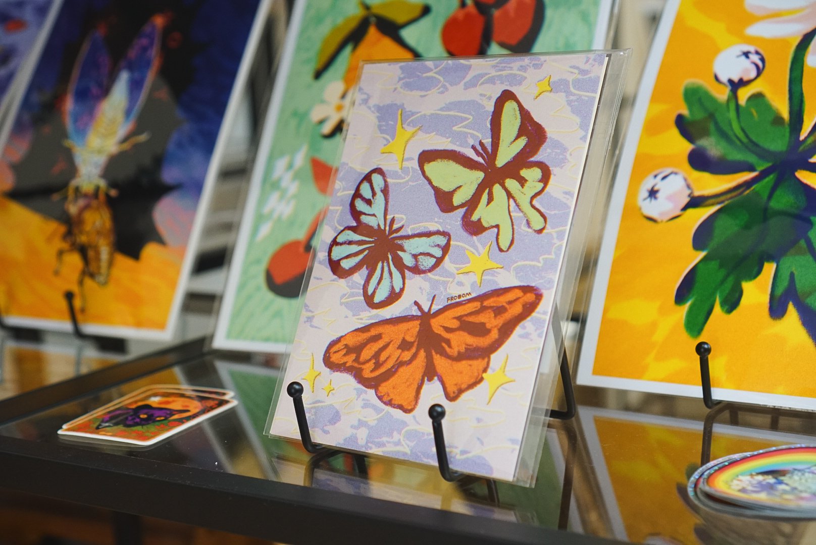 Colorful artwork of butterflies and stars on a display stand at an art exhibit.