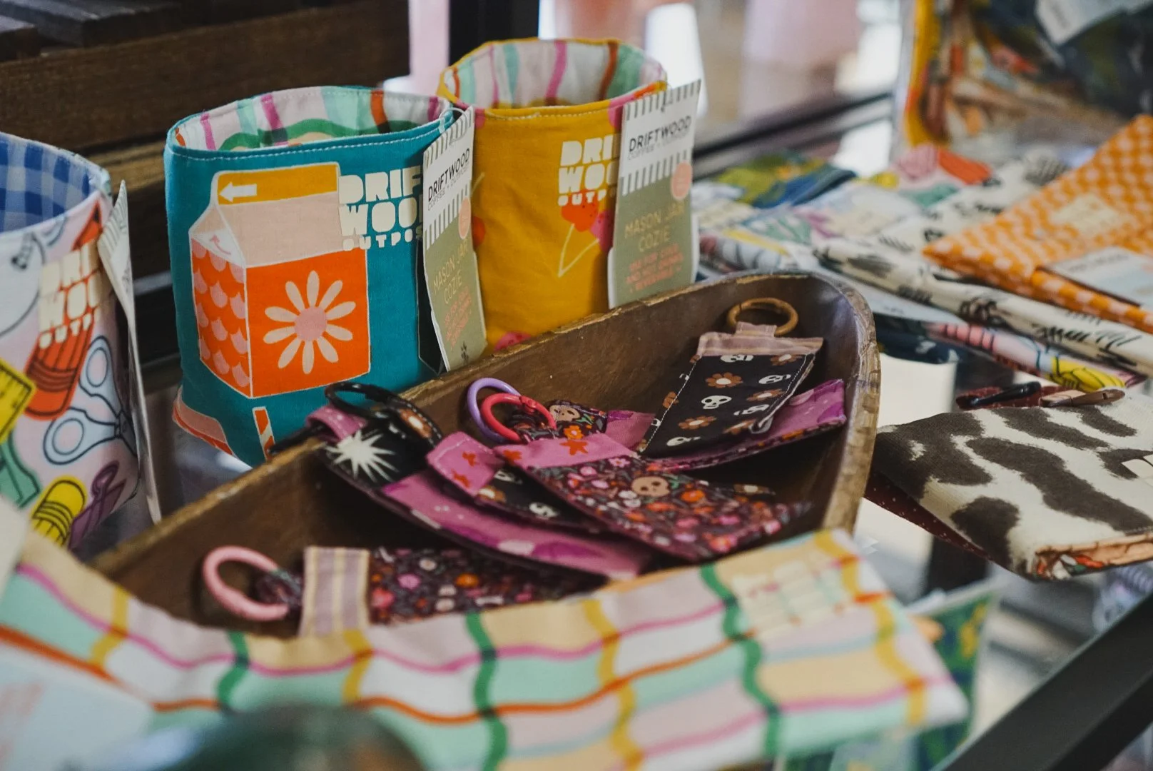 Colorful fabric mason jar cozies displayed on a wooden shelf, each with a label and a different fabric pattern.