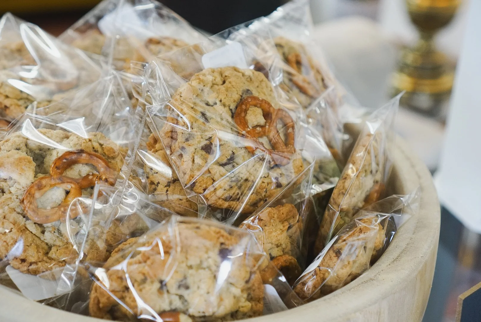 A close-up of several chocolate chip cookies in clear plastic wrapping inside a wooden container.