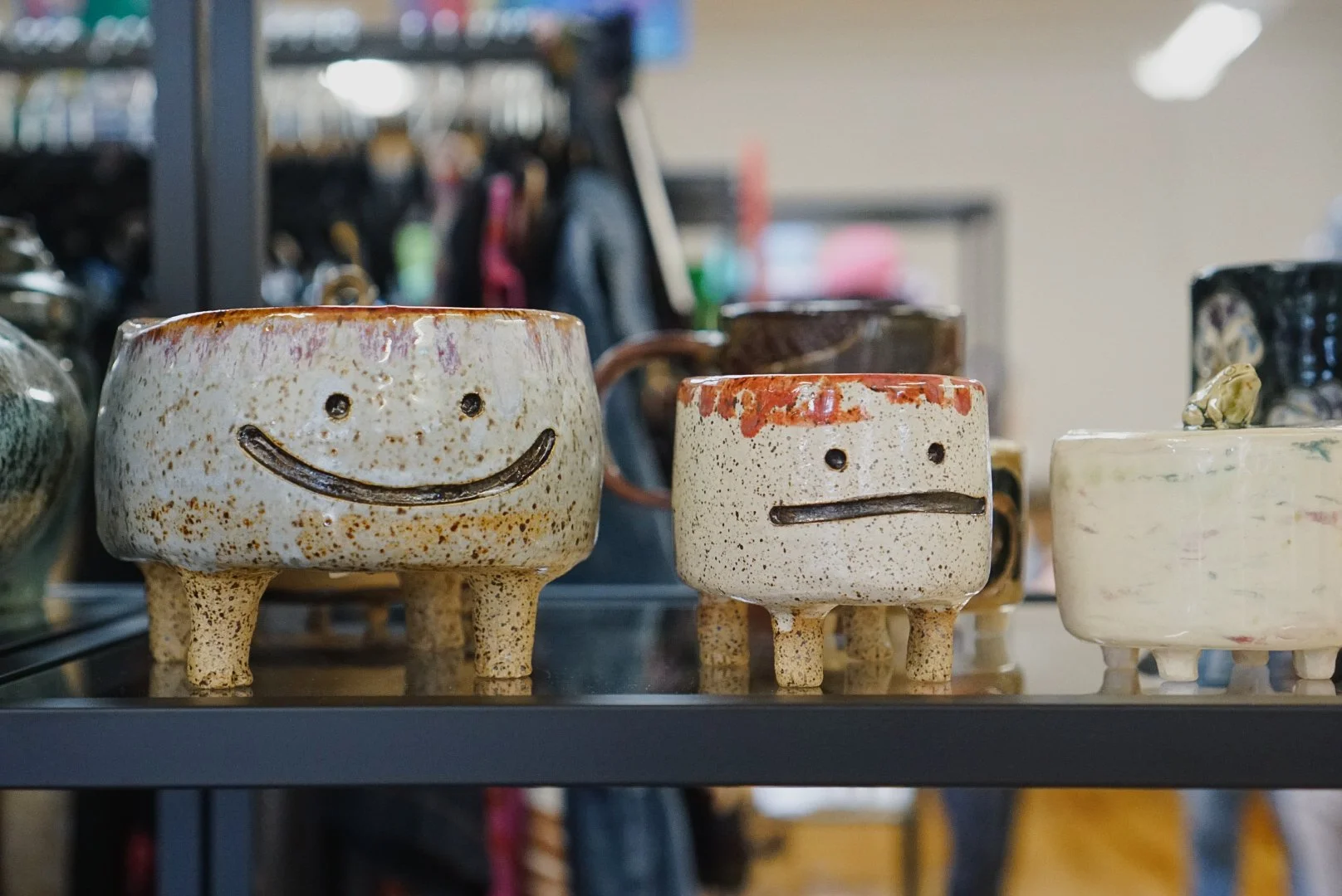 Ceramic cups with smiley and neutral faces, displayed on a shelf in a store.