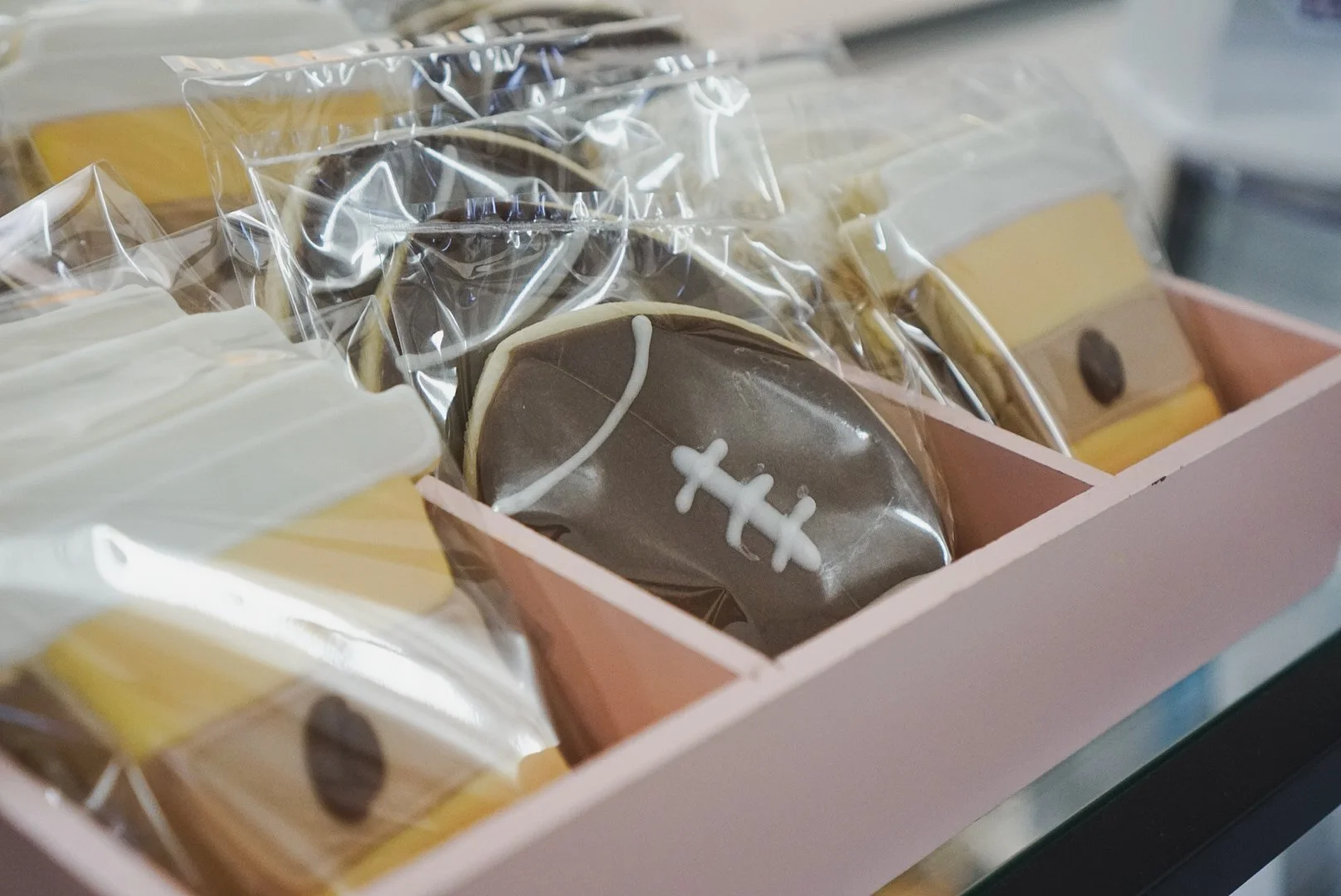 Pink box containing decorated cookies, with one cookie decorated as a football, wrapped in plastic