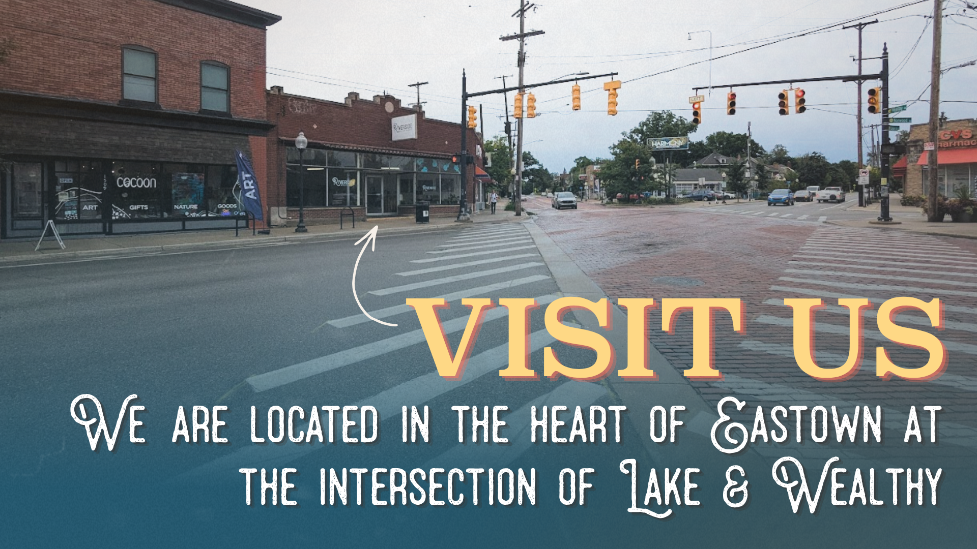 A street view in Easttown with brick buildings, traffic lights, cars, and pedestrians. Overlay text invites visitors to the area and explains its location at the intersection of Lake and Wealthy.