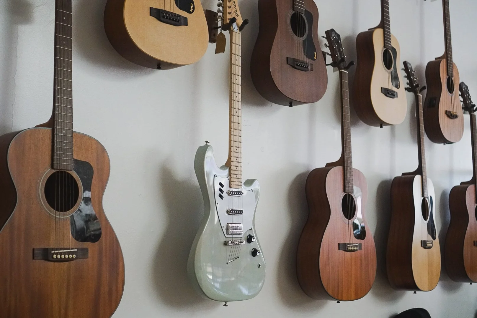 A wall filled with various acoustic and electric guitars hanging for display.