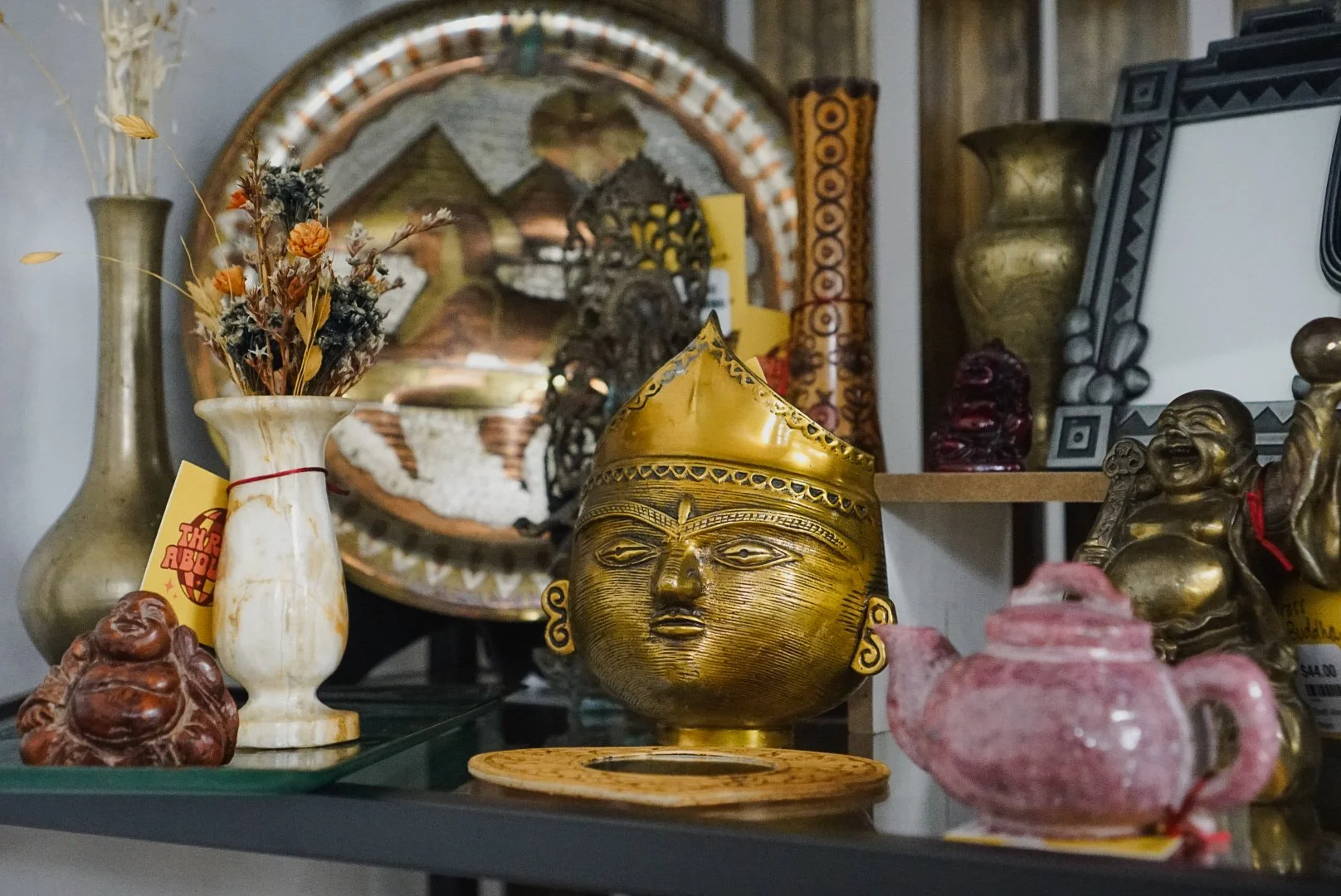 Various traditional and decorative Asian artifacts including a golden mask, vases, and statues arranged on shelves.