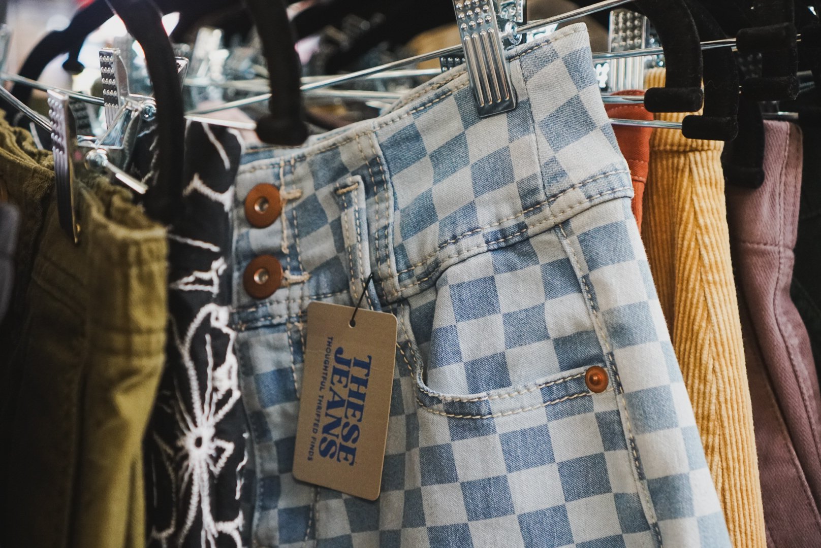 Clothes hanging on a rail, primarily jeans of various shades of blue and some white clothing, with wooden hangers.